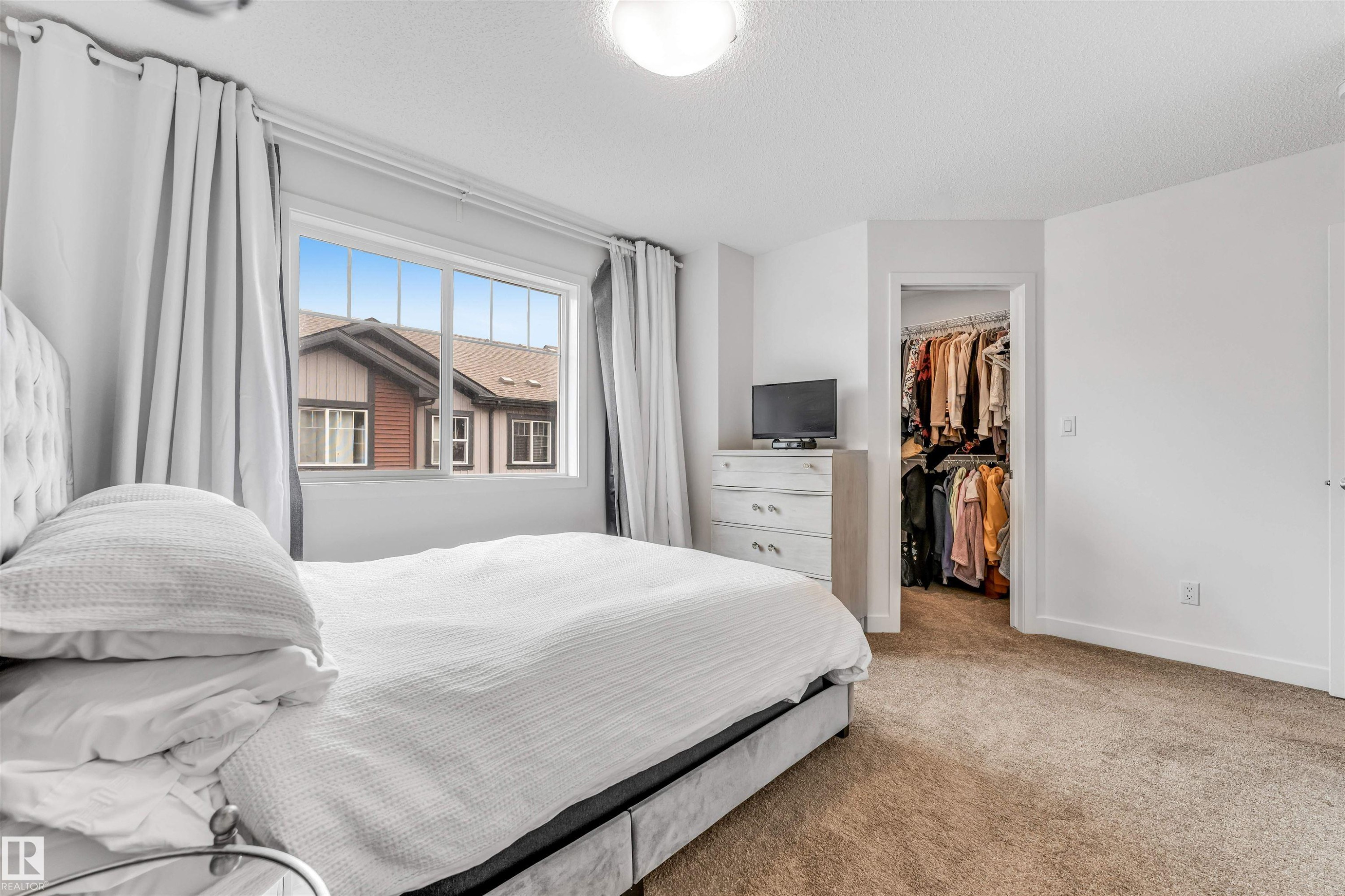 Bright bedroom featuring a large window, neutral carpeting, and a walk-in closet with built-in shelving - 116 3305 Orchards Link Sw, Edmonton, AB