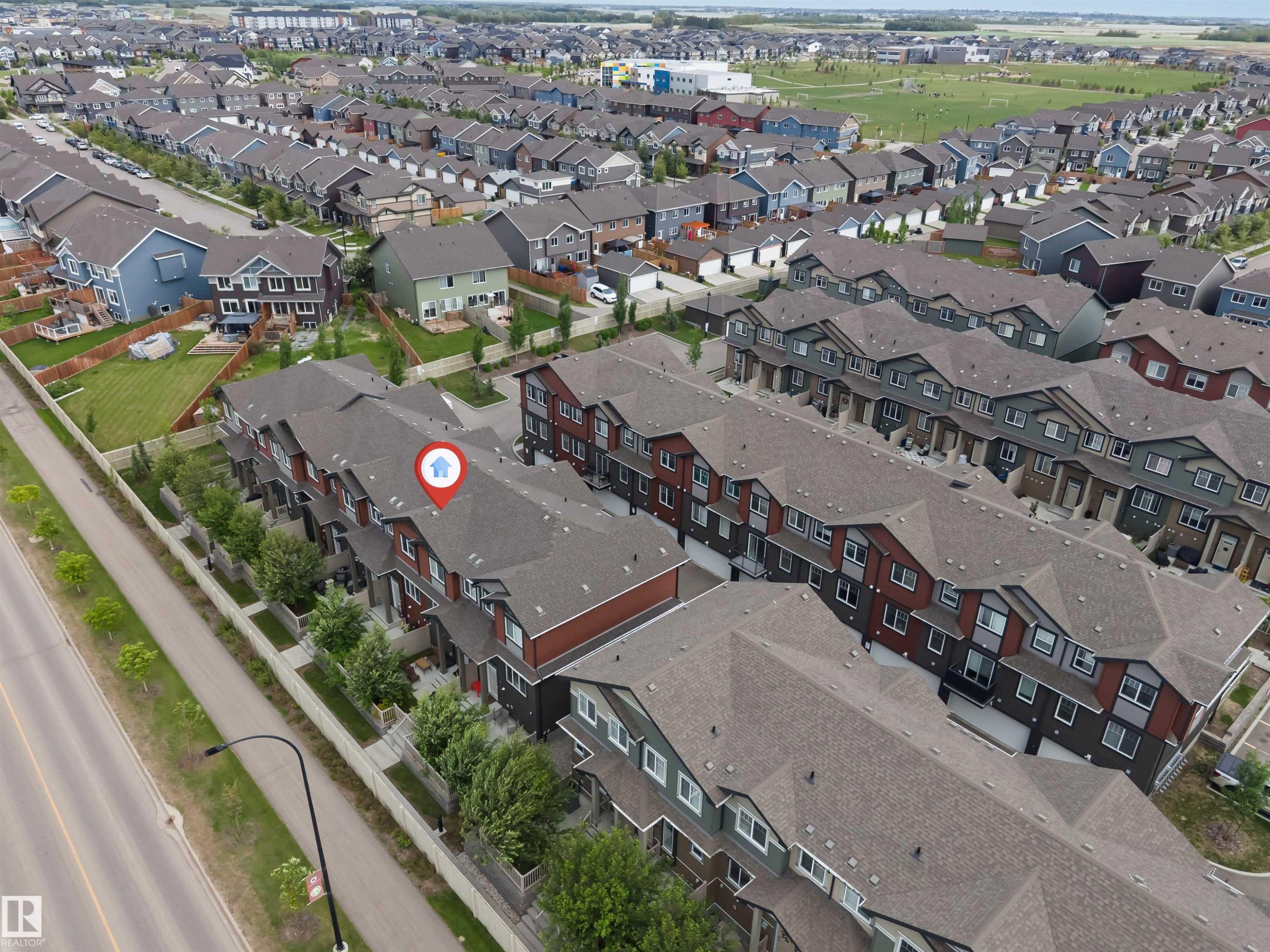 Aerial perspective showcasing a row of multi-level townhomes with dark shingled roofs and varied exterior finishes - 116 3305 Orchards Link Sw, Edmonton, AB