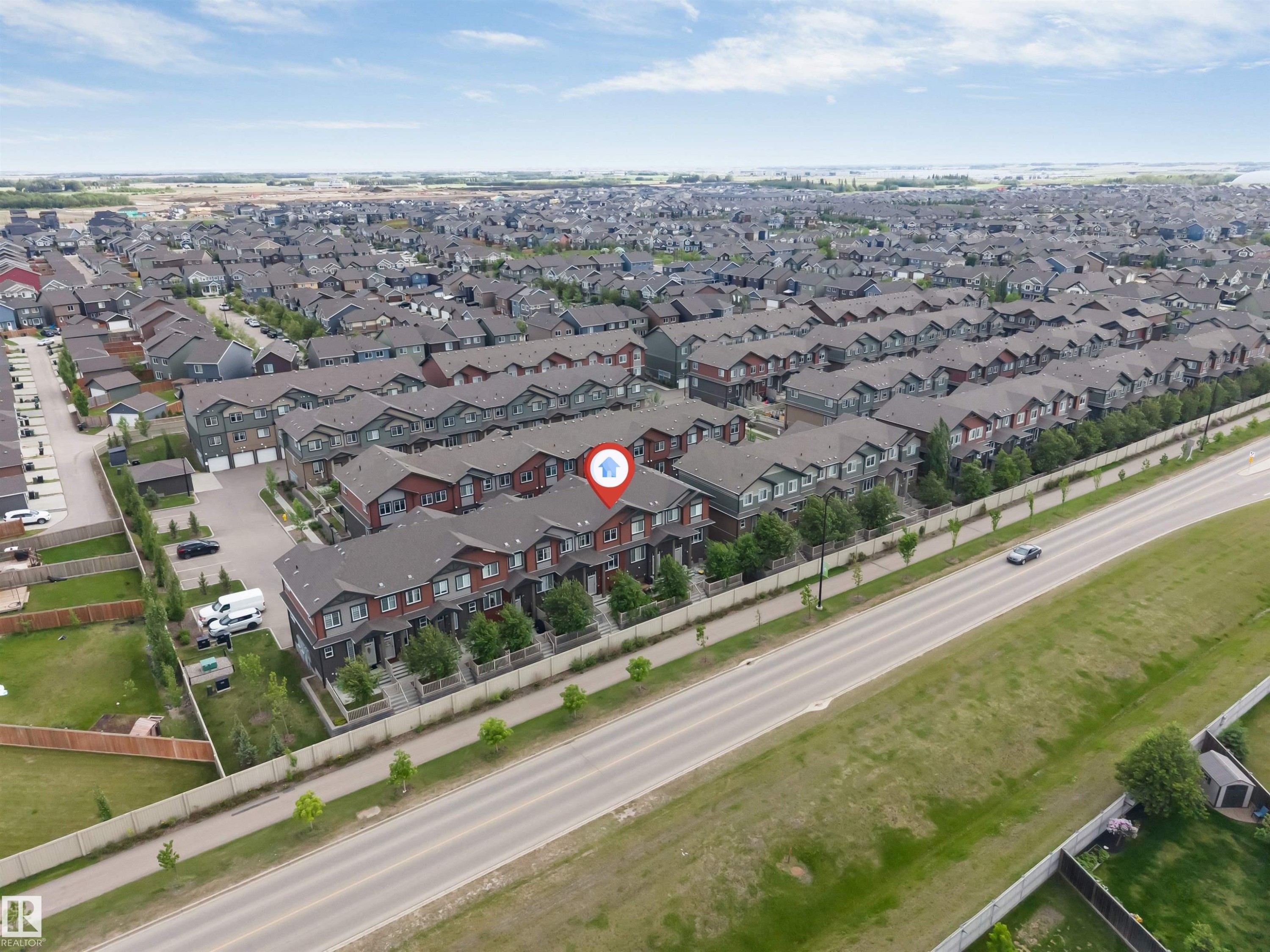 Aerial view showcasing a row of multi-story townhomes with dark roofs and varied exterior finishes - 116 3305 Orchards Link Sw, Edmonton, AB