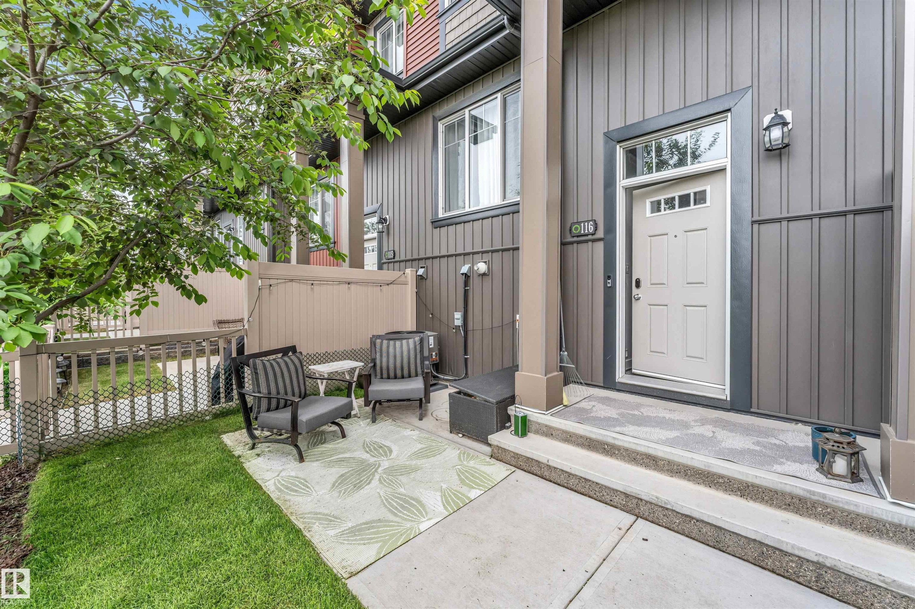 Vertical siding exterior with a light-colored entry door, featuring a transom window and integrated lighting - 116 3305 Orchards Link Sw, Edmonton, AB