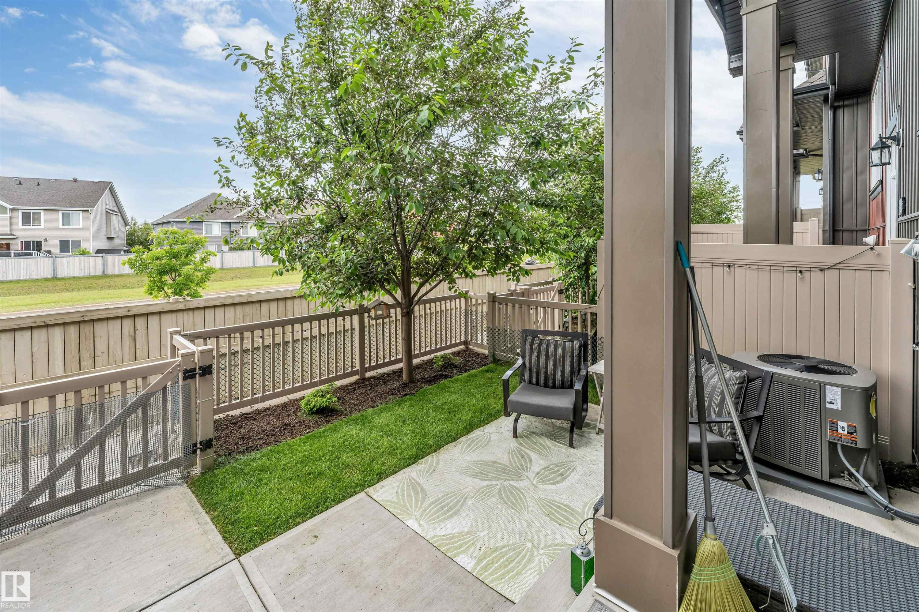 Paved patio area featuring concrete flooring, a small lawn, and a mature tree - 116 3305 Orchards Link Sw, Edmonton, AB