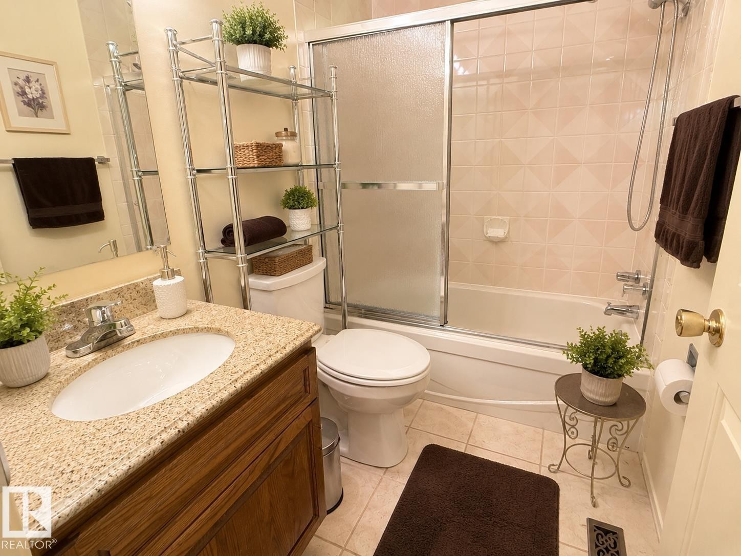 Bathroom with a white bathtub featuring a sliding glass shower door and light-toned tile surround - 1 Munro Court, Leduc, AB