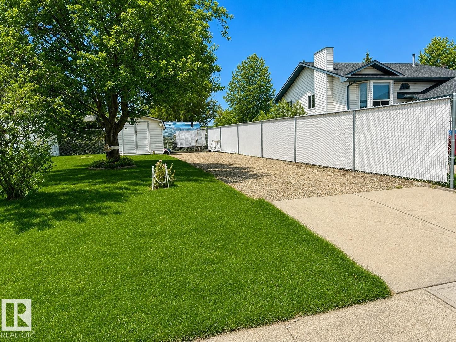 White chain-link fence with privacy slats bordering a gravel area - 1 Munro Court, Leduc, AB