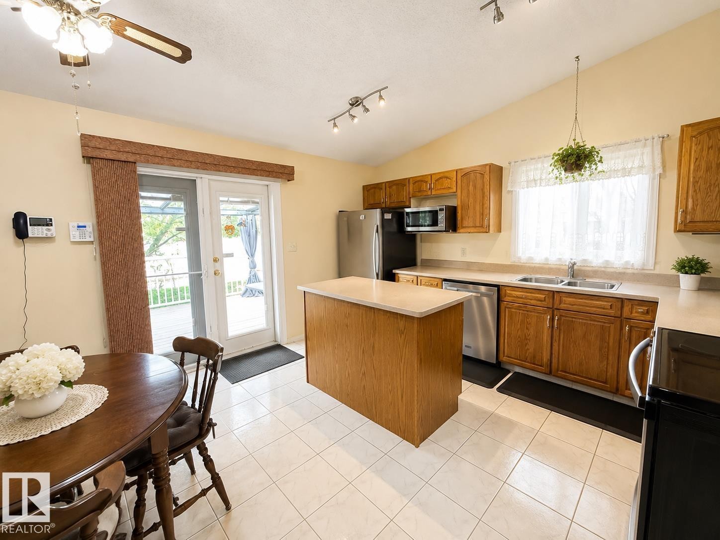 Kitchen featuring wood cabinetry, a center island with countertop, stainless steel appliances, and tile flooring - 1 Munro Court, Leduc, AB