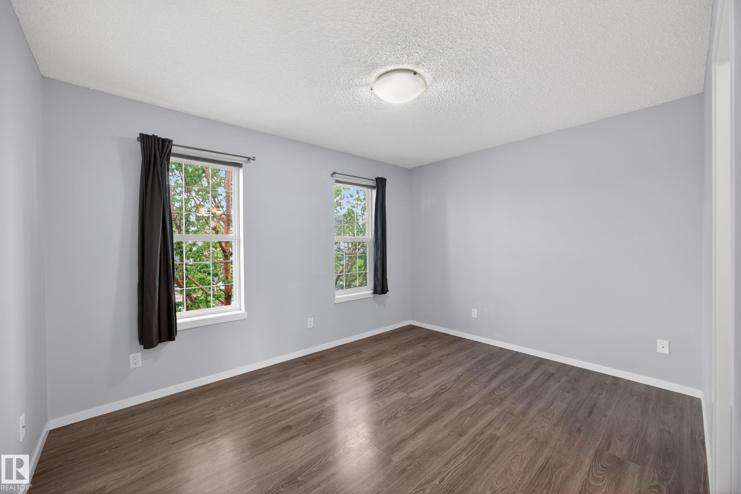Bright interior space featuring light gray walls, wood-finish flooring, two windows with white trim, and a ceiling-mounted light fixture - 3634 12 Street, Edmonton, AB