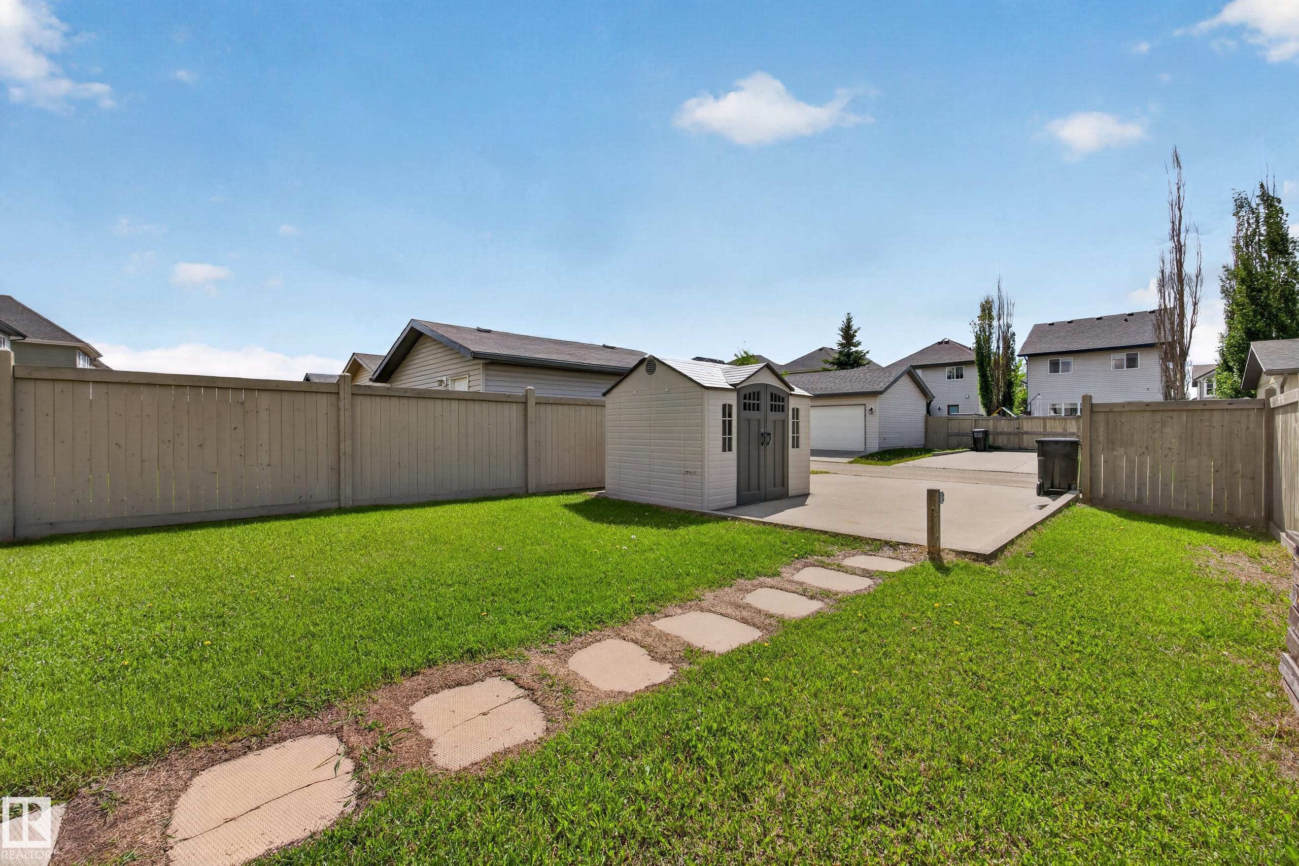 Spacious backyard featuring a manicured lawn, a concrete patio, a storage shed, a wood fence, and stepping stones - 3634 12 Street, Edmonton, AB