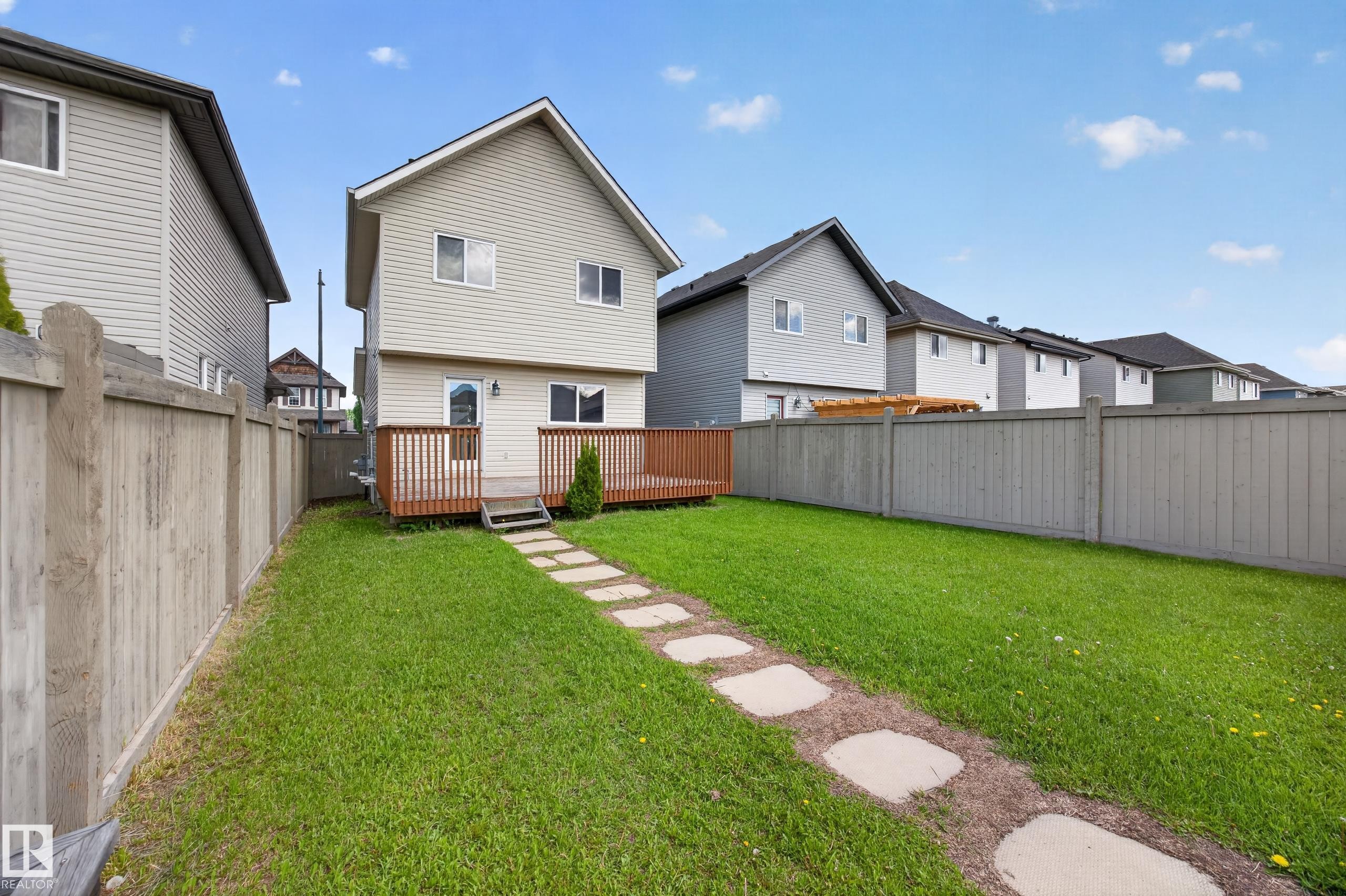 Expansive backyard featuring a manicured lawn, a stone paver pathway, and a large wooden deck - 3634 12 Street, Edmonton, AB