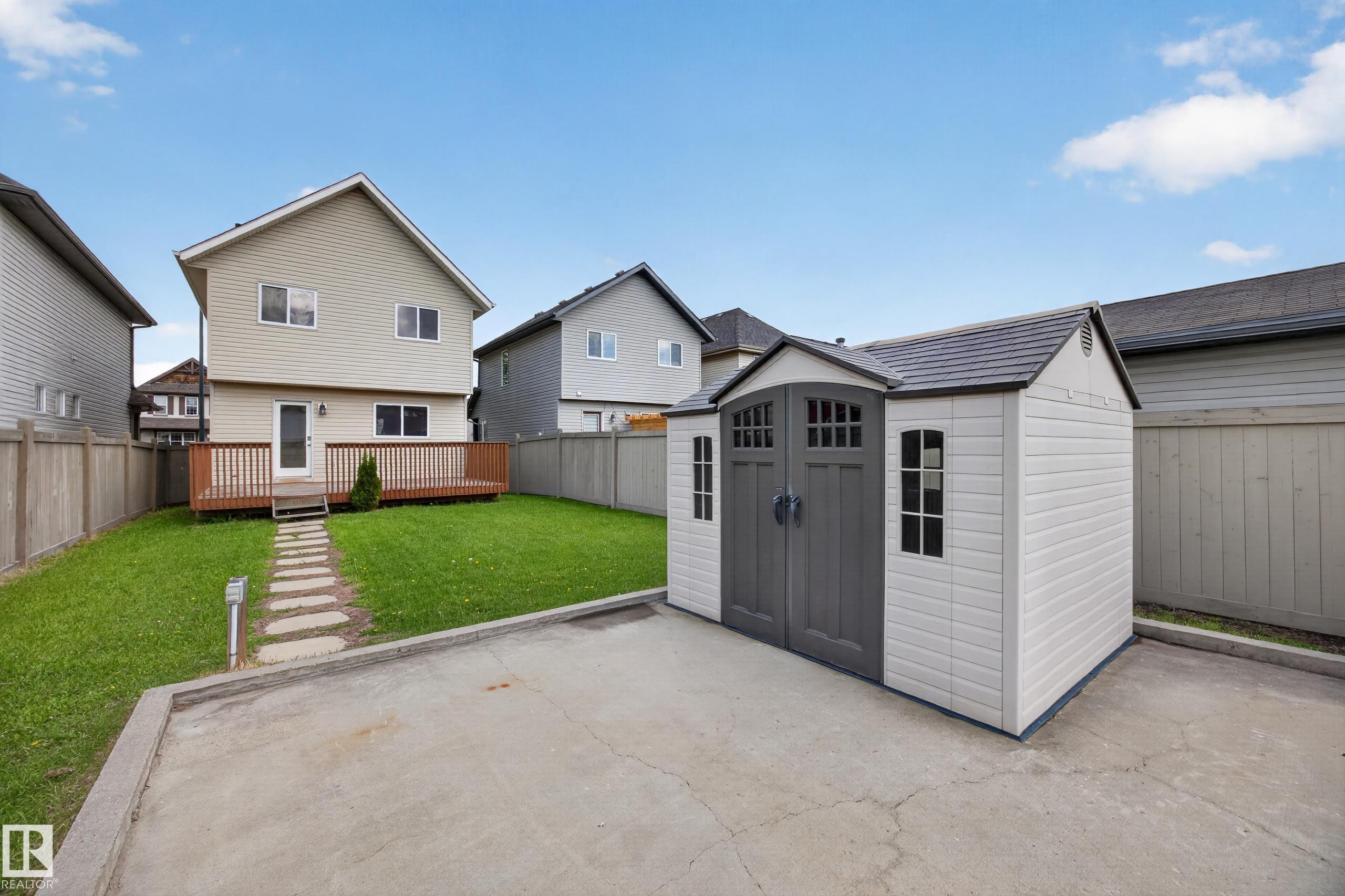 Backyard featuring a spacious wood deck, stone pathway, and a detached storage shed with double doors and window details - 3634 12 Street, Edmonton, AB