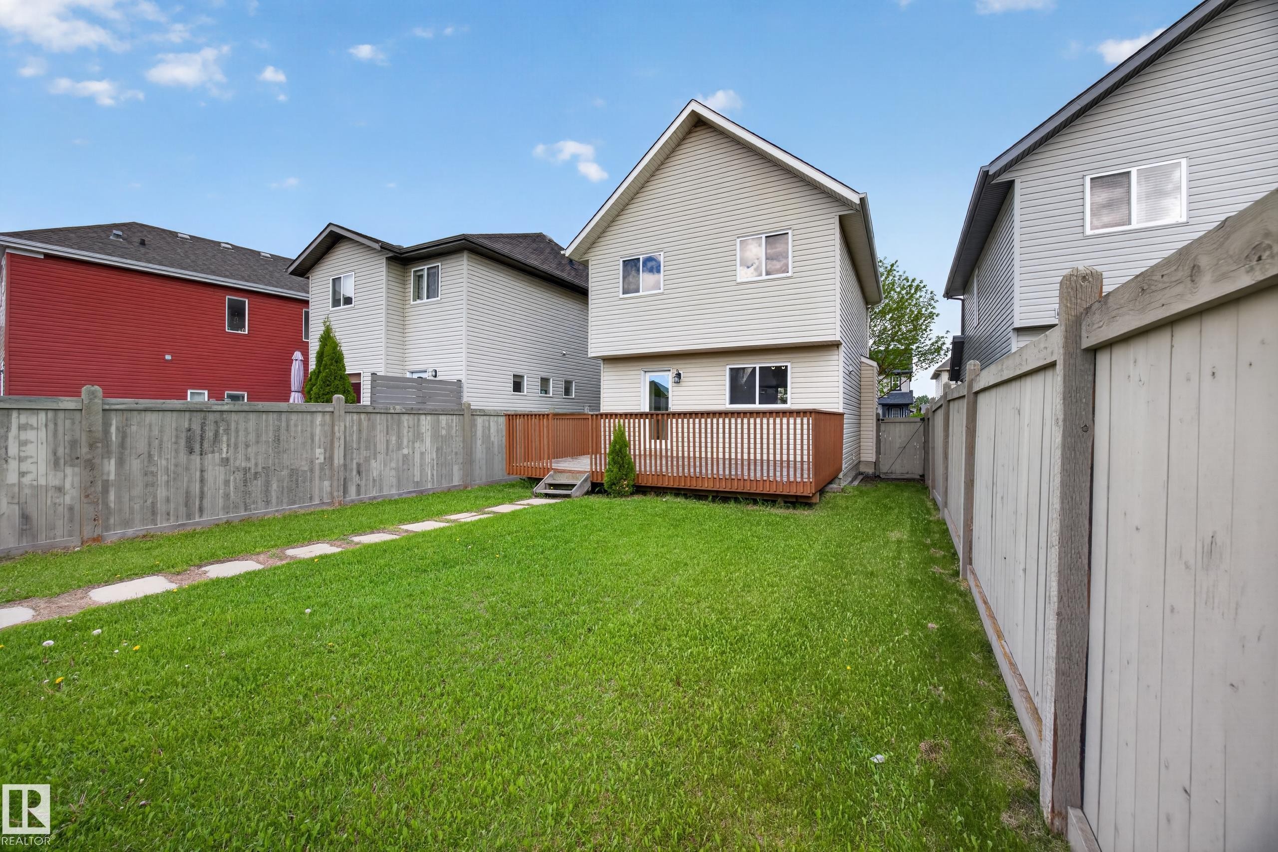 Expansive backyard featuring a manicured lawn, a full-width wood deck with railing, and a stone path - 3634 12 Street, Edmonton, AB