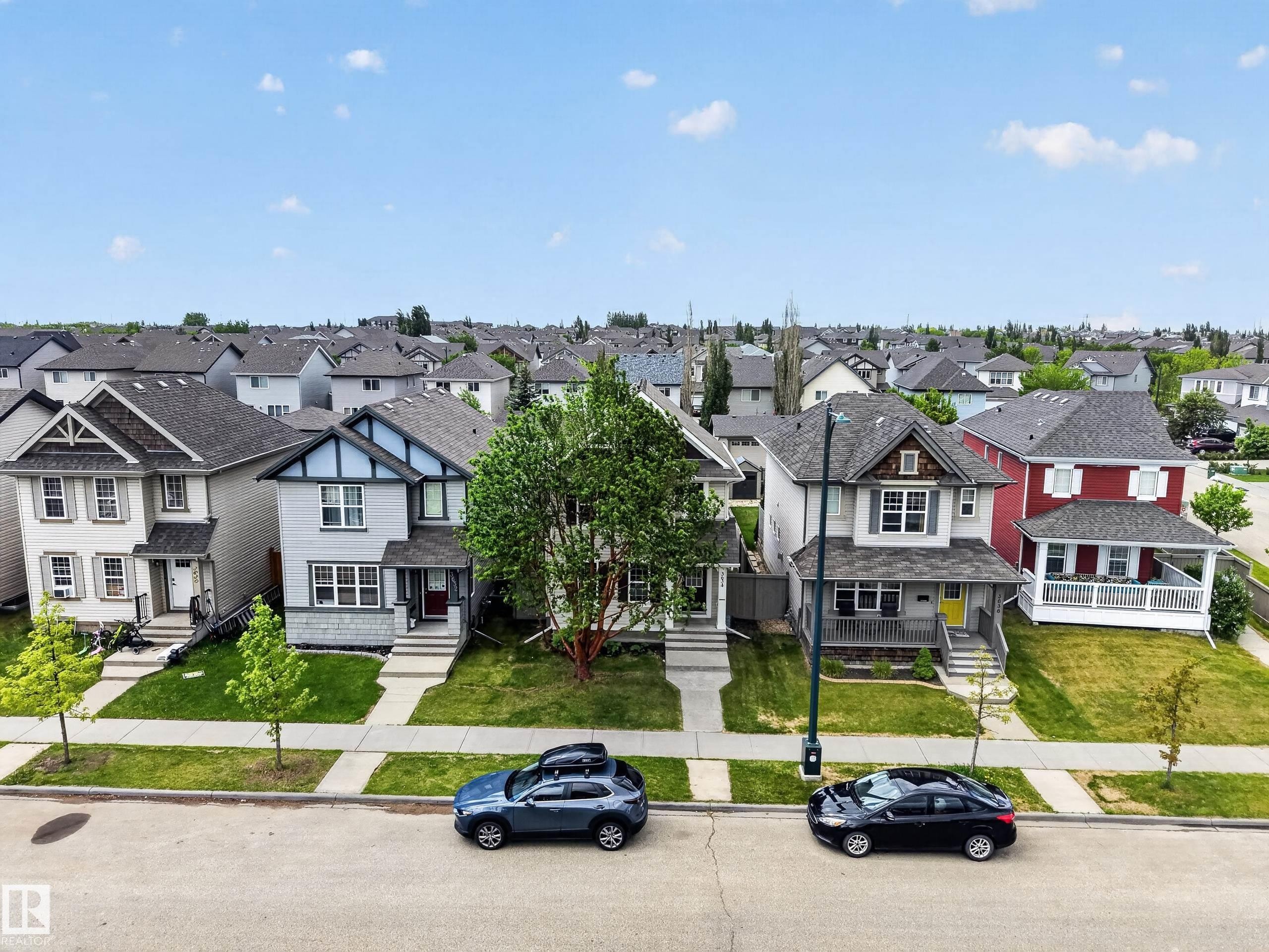 Residential streetscape featuring a consistent architectural style across multiple properties, manicured green lawns, and established trees - 3634 12 Street, Edmonton, AB
