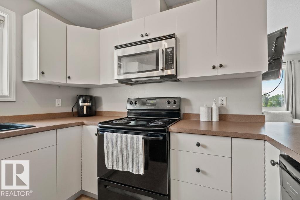 Kitchen featuring white cabinetry, a stainless steel over-the-range microwave, a black electric range, and laminate countertops - 232 4309 33 Street, Stony Plain, AB
