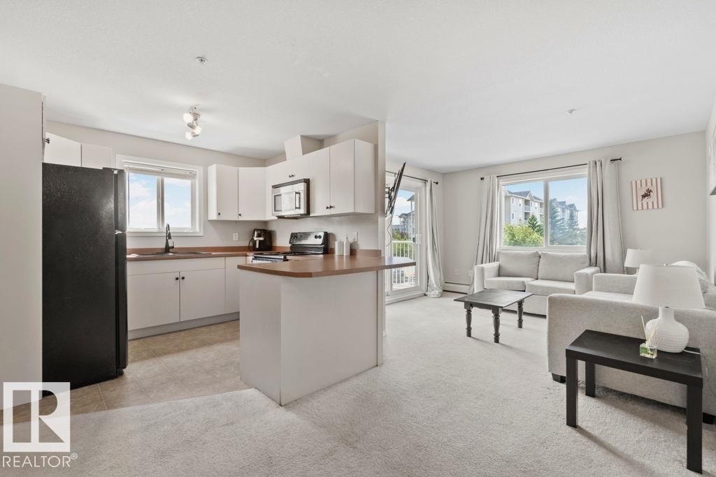 Open-concept living space featuring a kitchen with white cabinetry and dark countertops, a black refrigerator, and an included microwave - 232 4309 33 Street, Stony Plain, AB