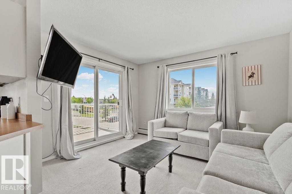 Bright open-concept living area featuring light-toned walls, neutral carpeting, and a sliding glass door providing outdoor access - 232 4309 33 Street, Stony Plain, AB