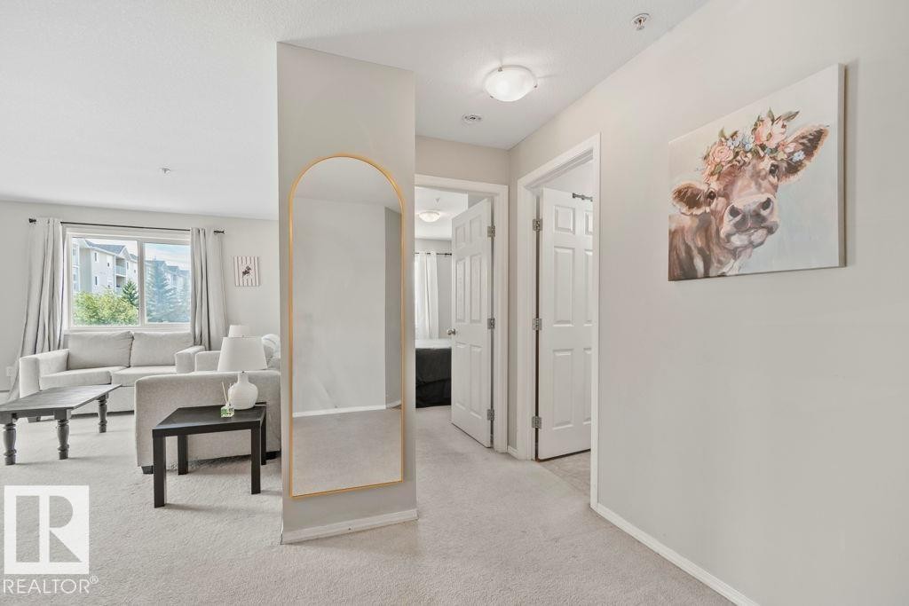 Carpeted living area featuring a large window, a partial wall, and light-colored walls - 232 4309 33 Street, Stony Plain, AB