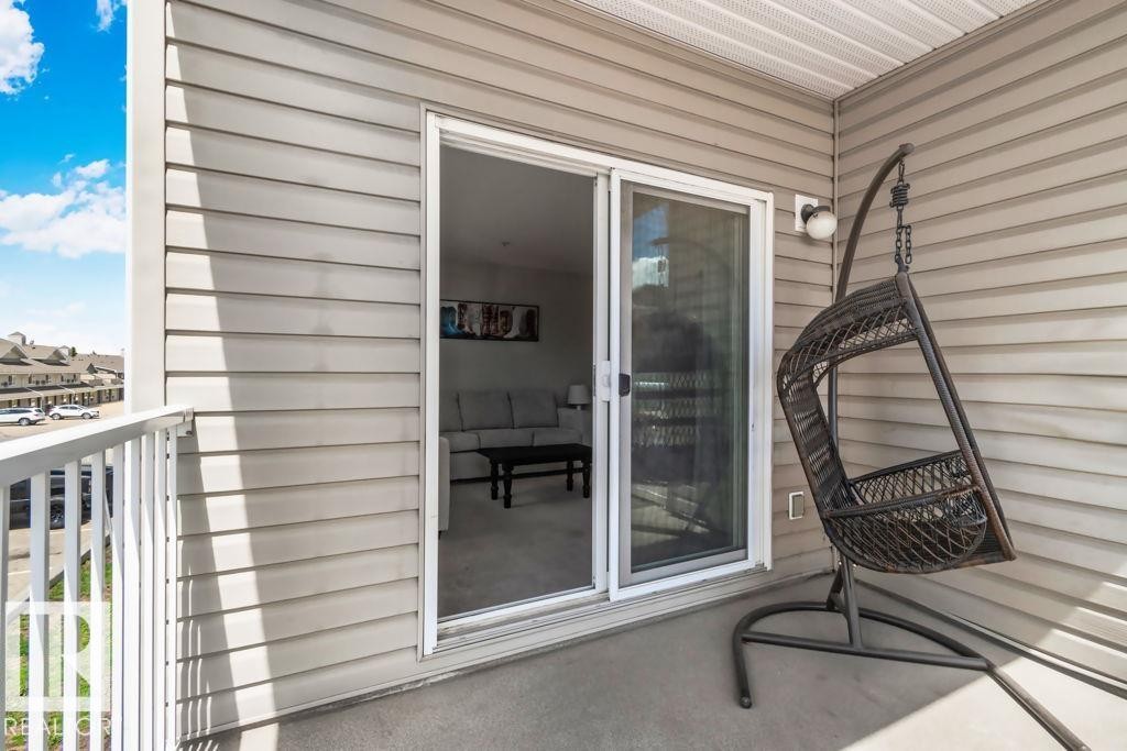 Outdoor balcony featuring horizontal siding, a sliding glass door, a white railing, and a textured concrete floor - 232 4309 33 Street, Stony Plain, AB