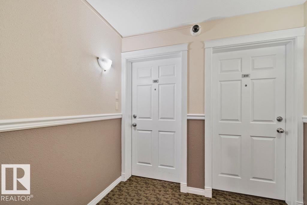 Entryway featuring two paneled doors with chrome hardware, a two-tone wall finish with chair rail molding, and a wall-mounted sconce - 232 4309 33 Street, Stony Plain, AB