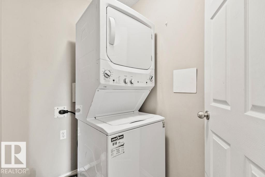 Laundry area featuring a white stacked washer and dryer, light neutral wall paint, and a white paneled door with a brushed nickel knob - 232 4309 33 Street, Stony Plain, AB