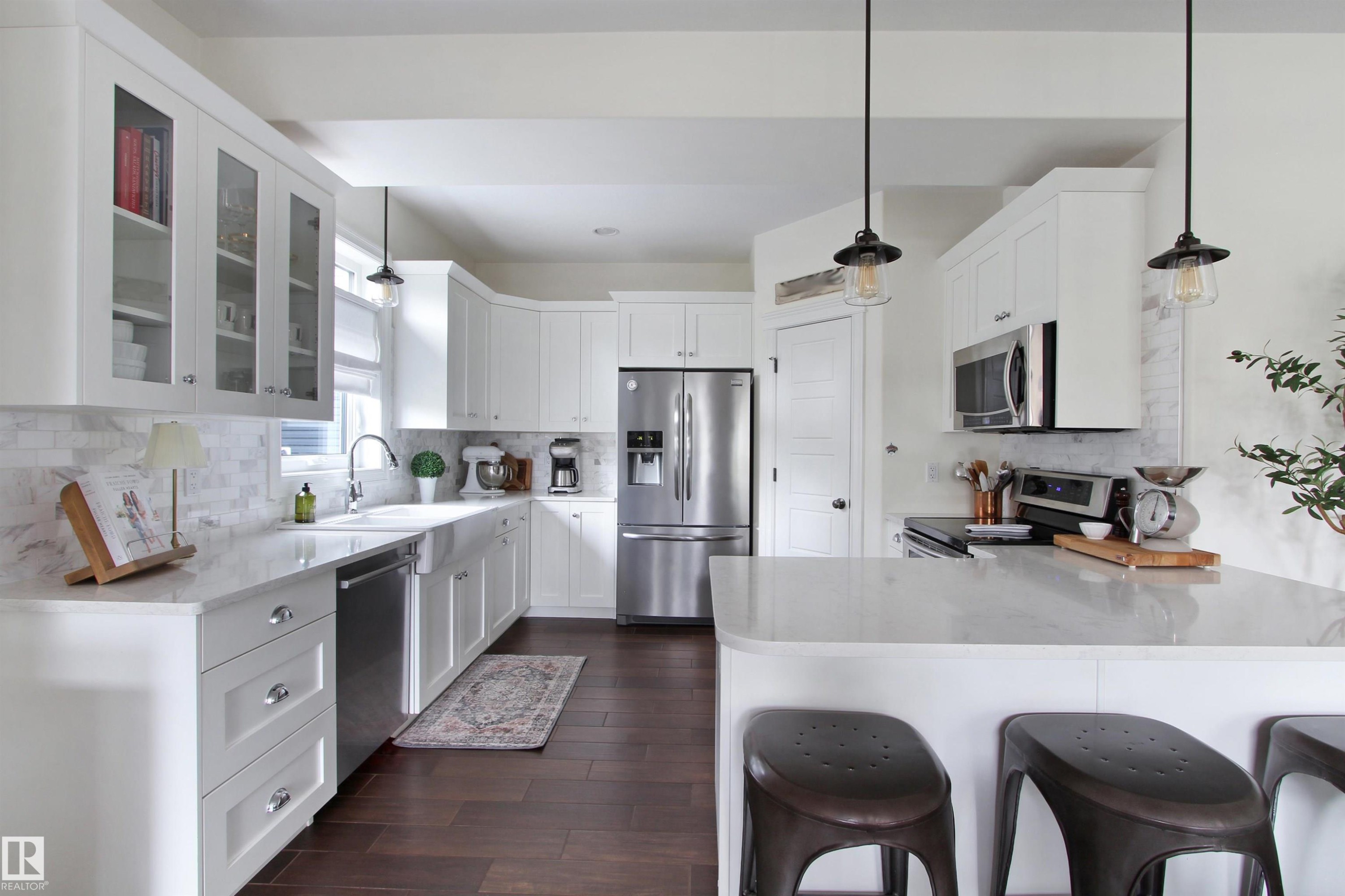 Bright kitchen featuring white cabinetry, stainless steel appliances, wood-finish flooring, a farmhouse sink, and pendant lighting - 34 Falcon Road, Cold Lake, AB