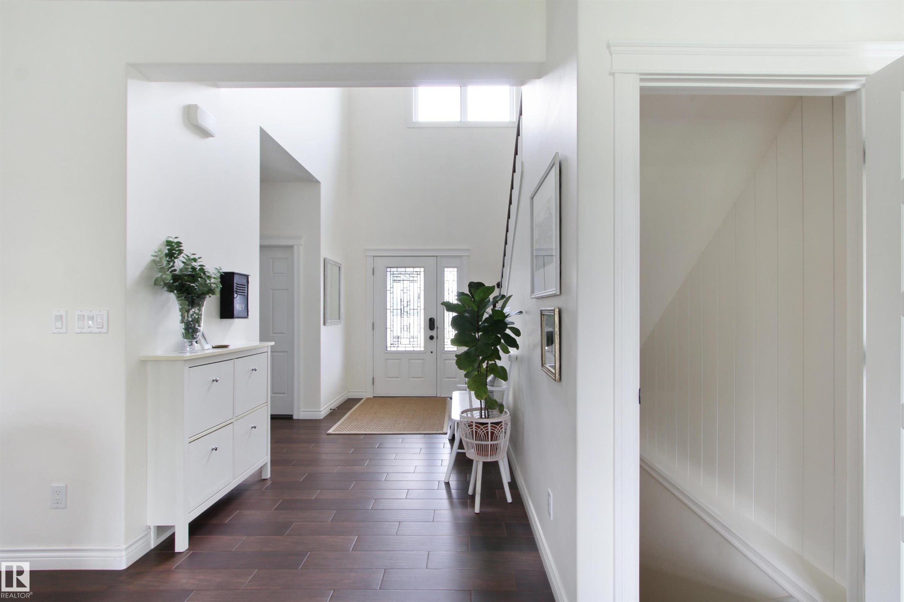 Two-story entryway featuring wood-finish flooring, a white paneled front door with glass inserts, and a transom window - 34 Falcon Road, Cold Lake, AB