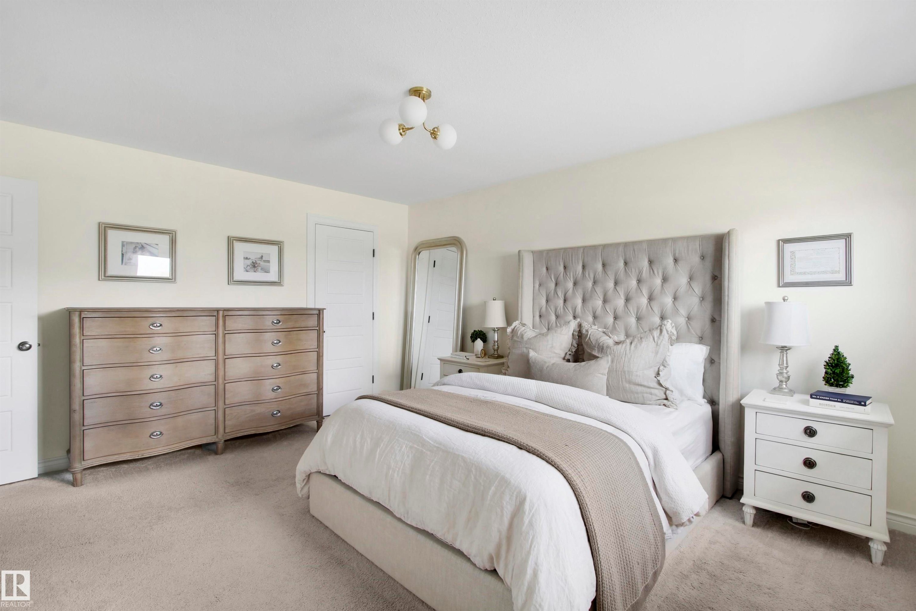 Carpeted room featuring a tufted upholstered headboard, a three-light semi-flush mount ceiling fixture, and a solid core interior door - 34 Falcon Road, Cold Lake, AB