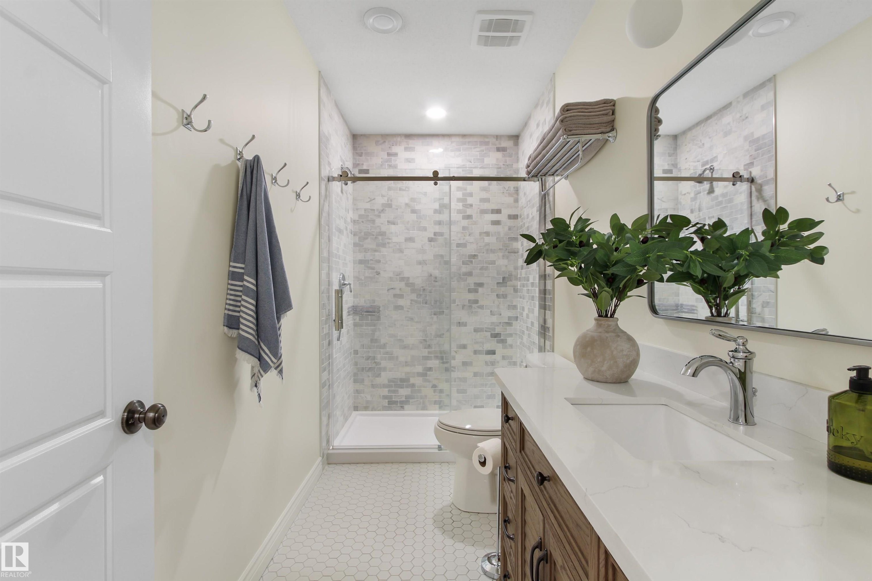 Bathroom featuring a wood-finish vanity with a white countertop and integrated sink, a large framed mirror, and a walk-in shower with glass enclosure and mosaic tile surround - 34 Falcon Road, Cold Lake, AB