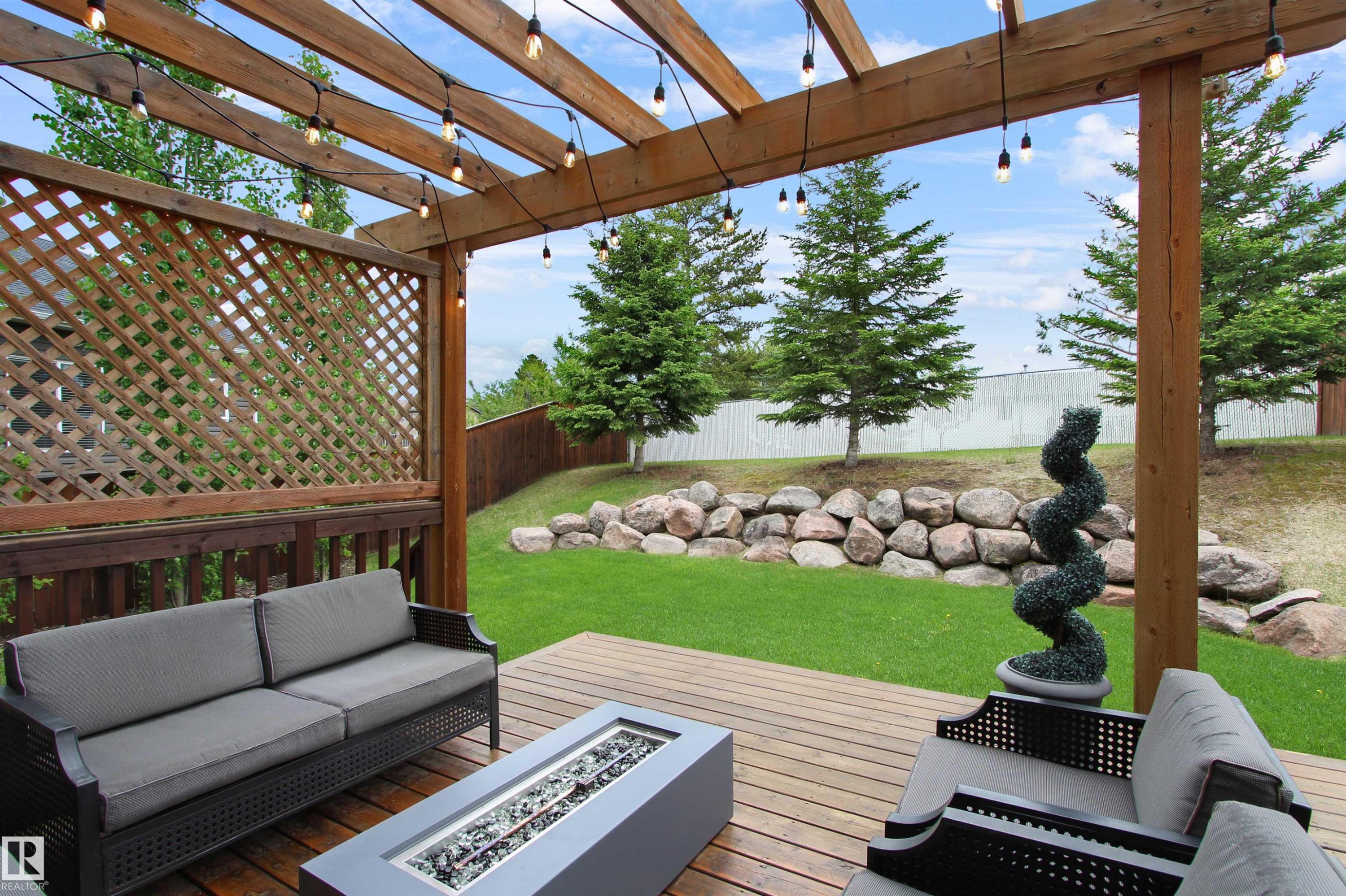 Expansive wood-finish deck with a built-in pergola featuring string lighting - 34 Falcon Road, Cold Lake, AB