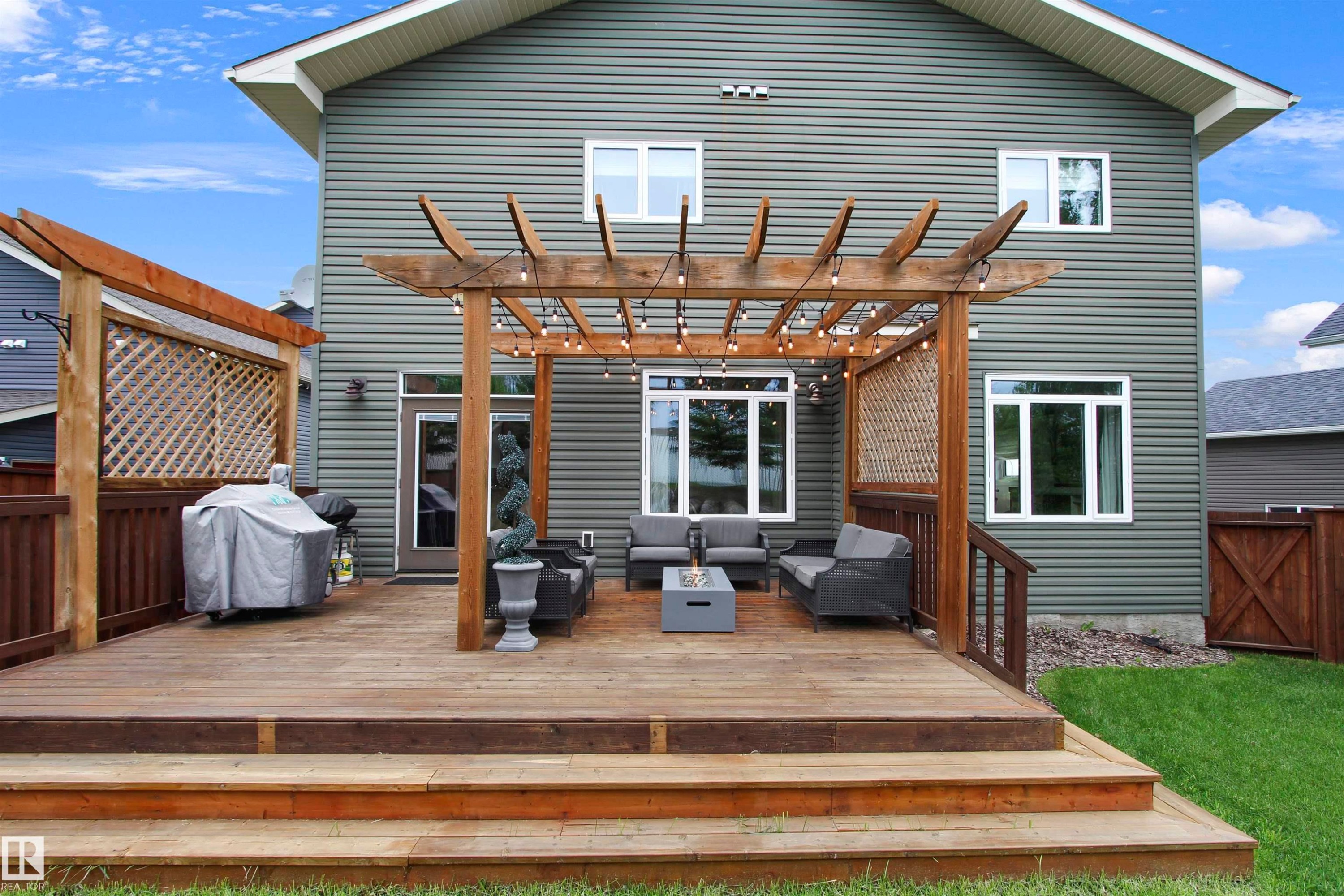 Multi-level wood deck featuring a pergola, privacy lattice, and steps leading to a grassed area - 34 Falcon Road, Cold Lake, AB