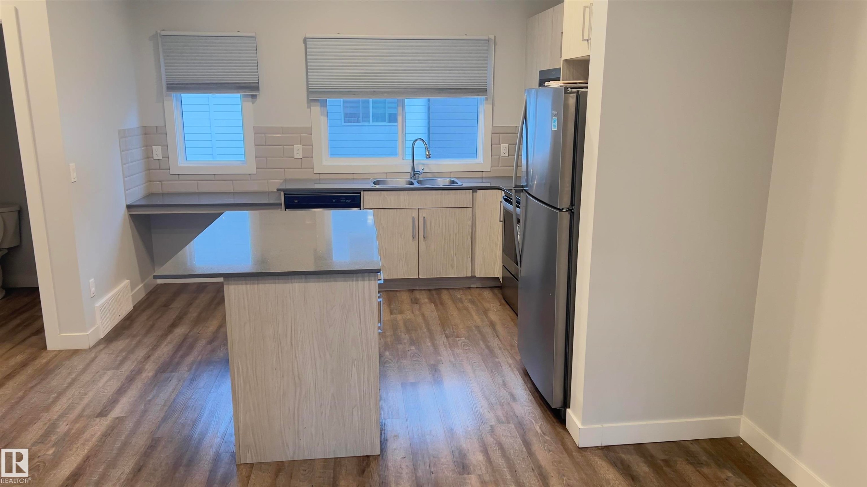Modern kitchen with wood-finish flooring, light wood-grain cabinetry, stainless steel appliances, and a central island with a contrasting countertop - 90 804 Welsh Drive, Edmonton, AB