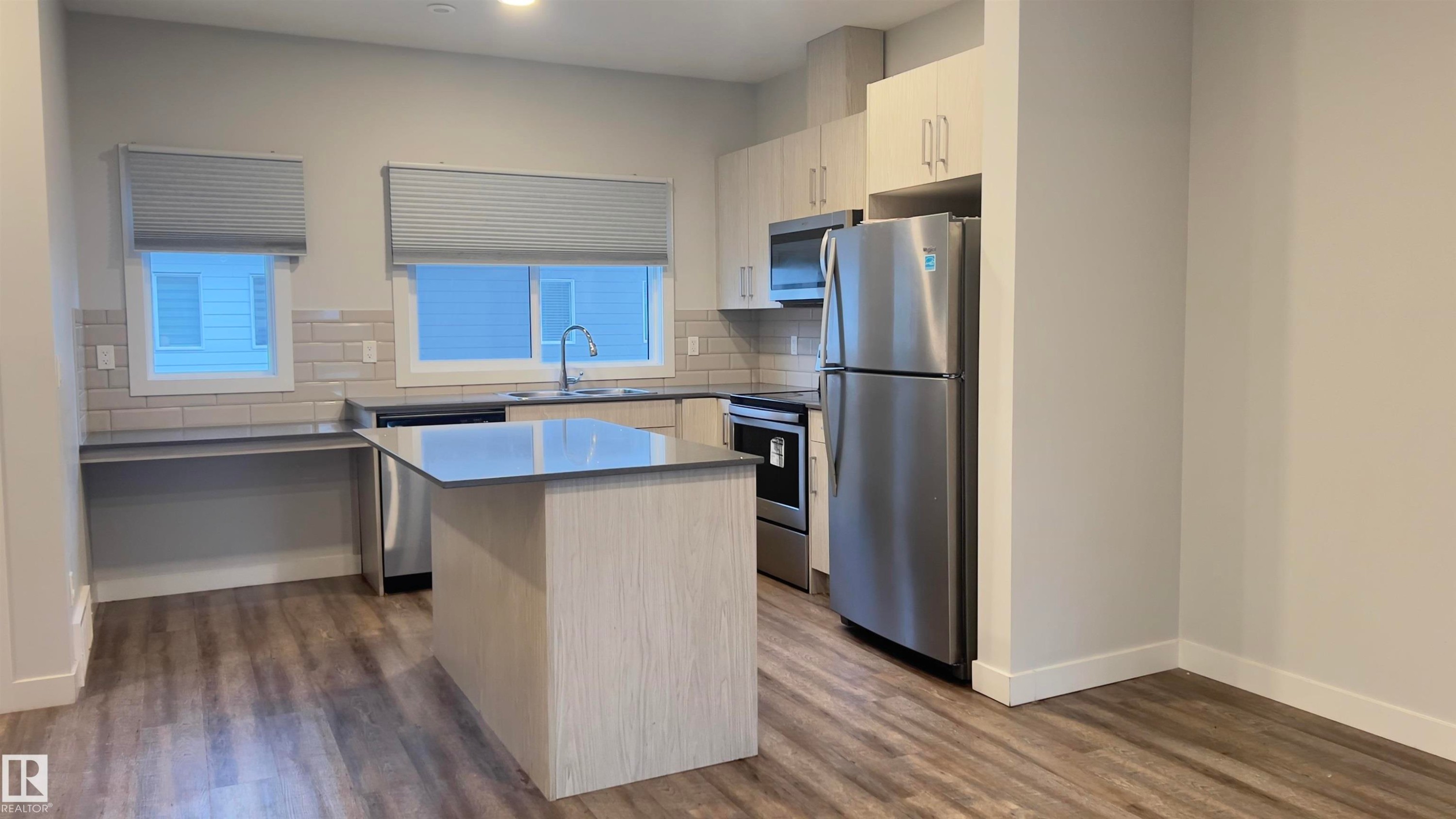 Kitchen featuring a central island with countertop seating, stainless steel appliances, light wood-finish cabinetry, a subway tile backsplash, and wood-finish flooring - 90 804 Welsh Drive, Edmonton, AB