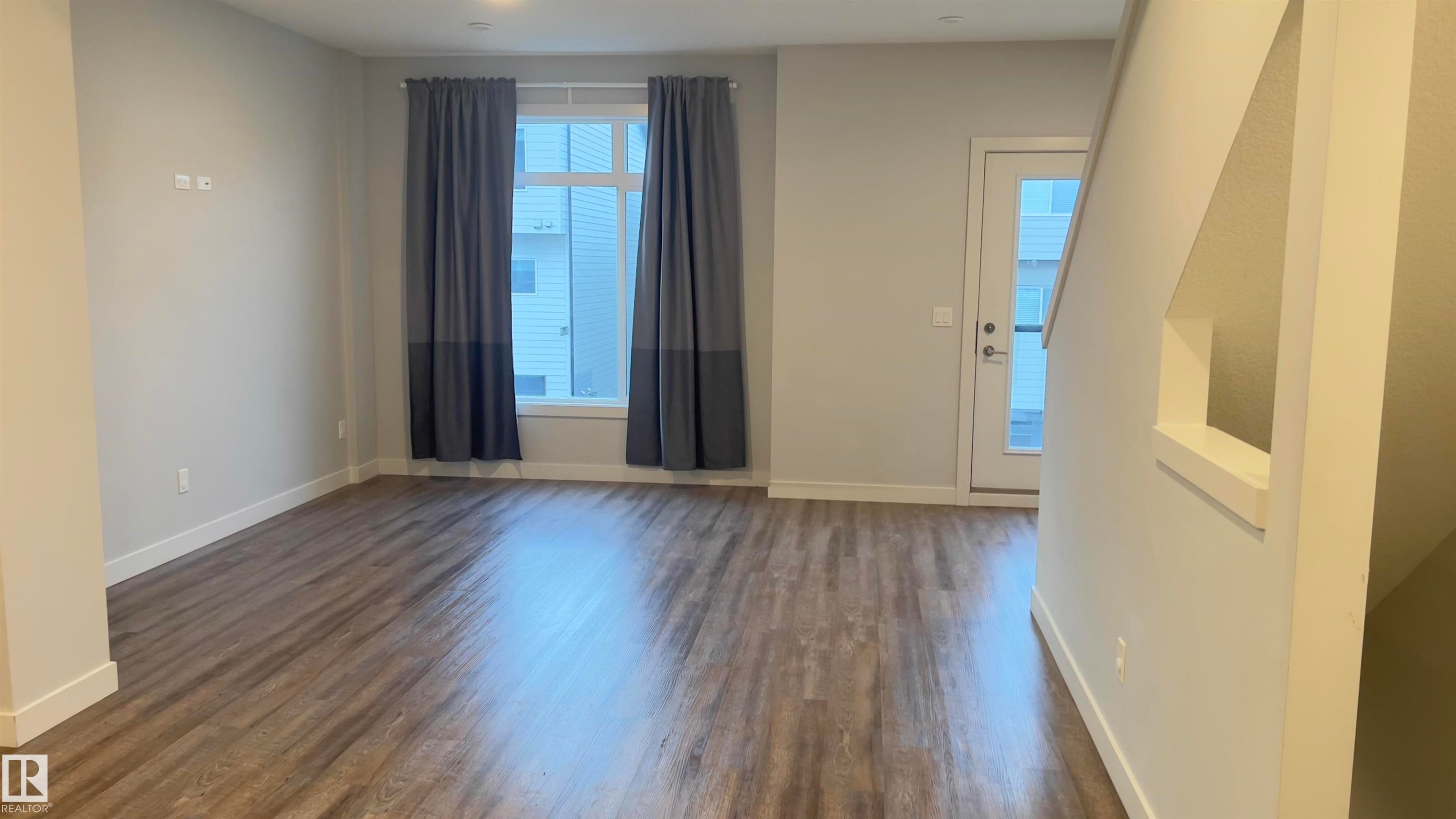 Spacious interior featuring wood-finish flooring, a large window with white framing, and a white entry door with glass paneling - 90 804 Welsh Drive, Edmonton, AB
