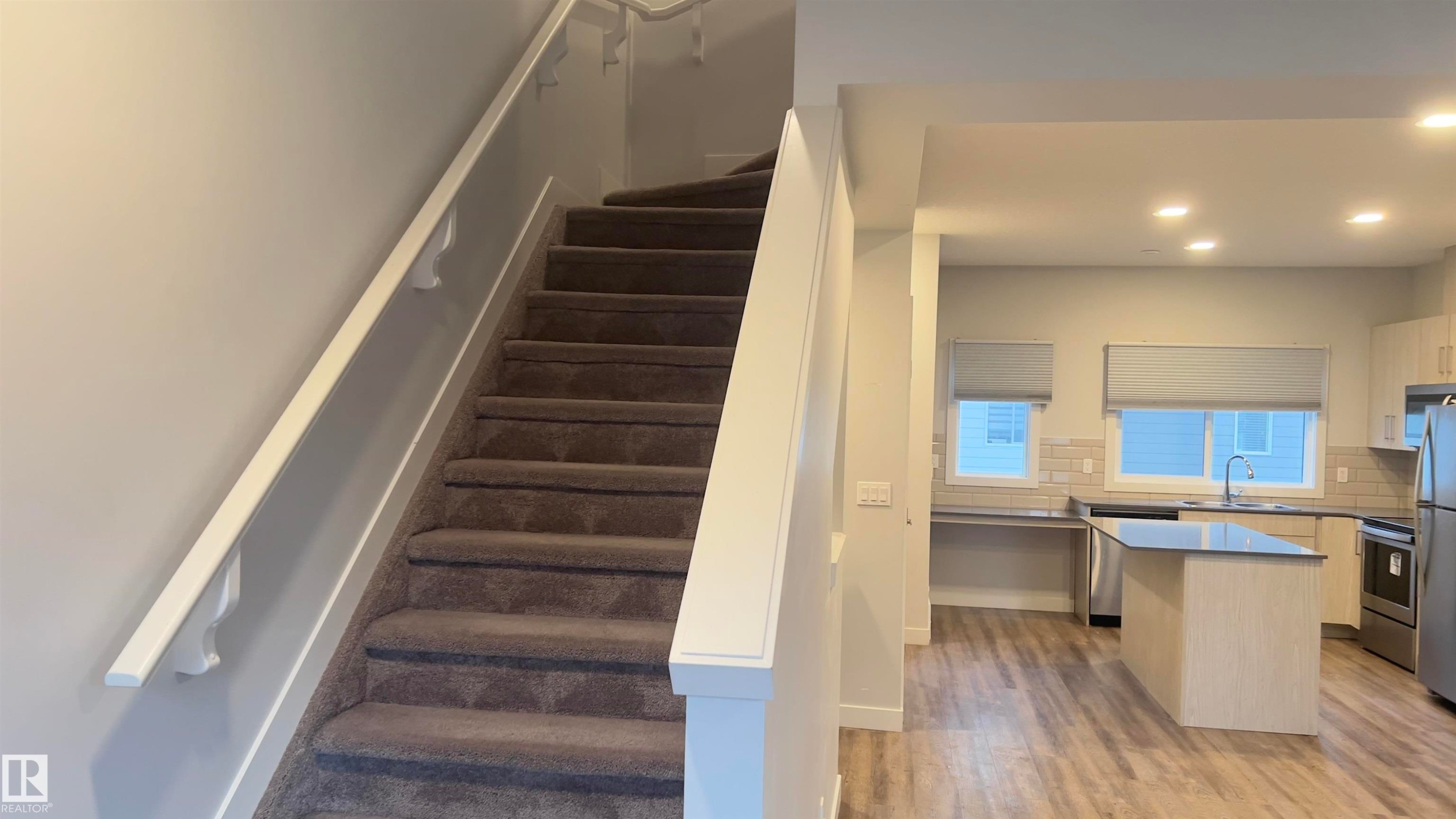 Carpeted staircase with white handrail leading to an open-concept kitchen - 90 804 Welsh Drive, Edmonton, AB