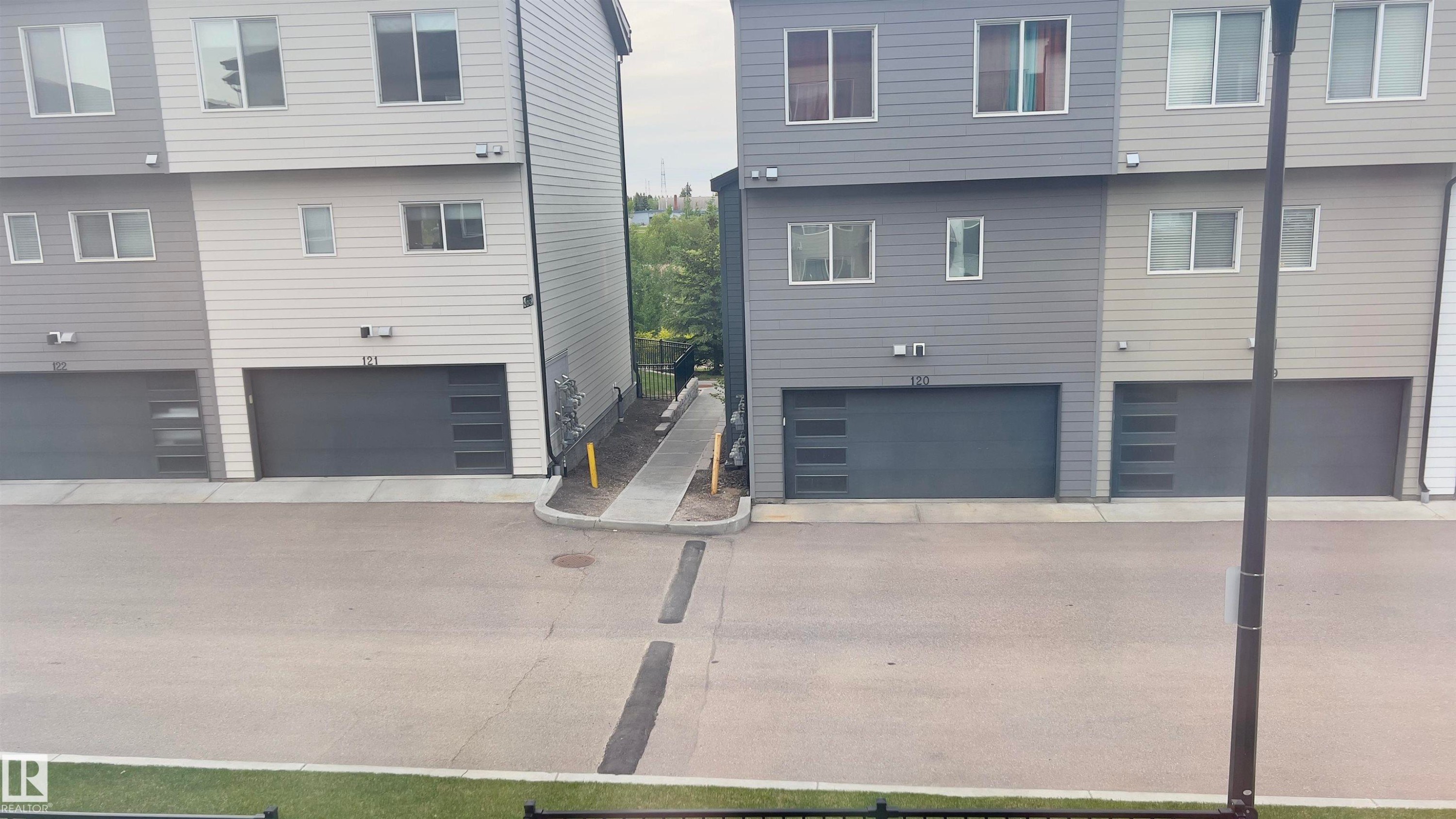 Modern multi-story facade featuring horizontal siding in varied gray tones, individual garages with contemporary door designs, multiple windows, and a paved drive - 90 804 Welsh Drive, Edmonton, AB