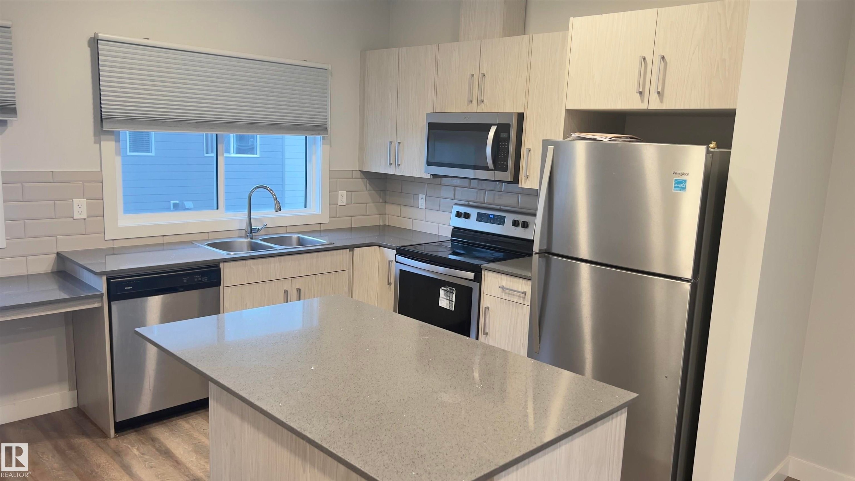 Modern kitchen featuring light wood-finish cabinetry, stainless steel appliances, a center island, and wood-finish flooring - 90 804 Welsh Drive, Edmonton, AB