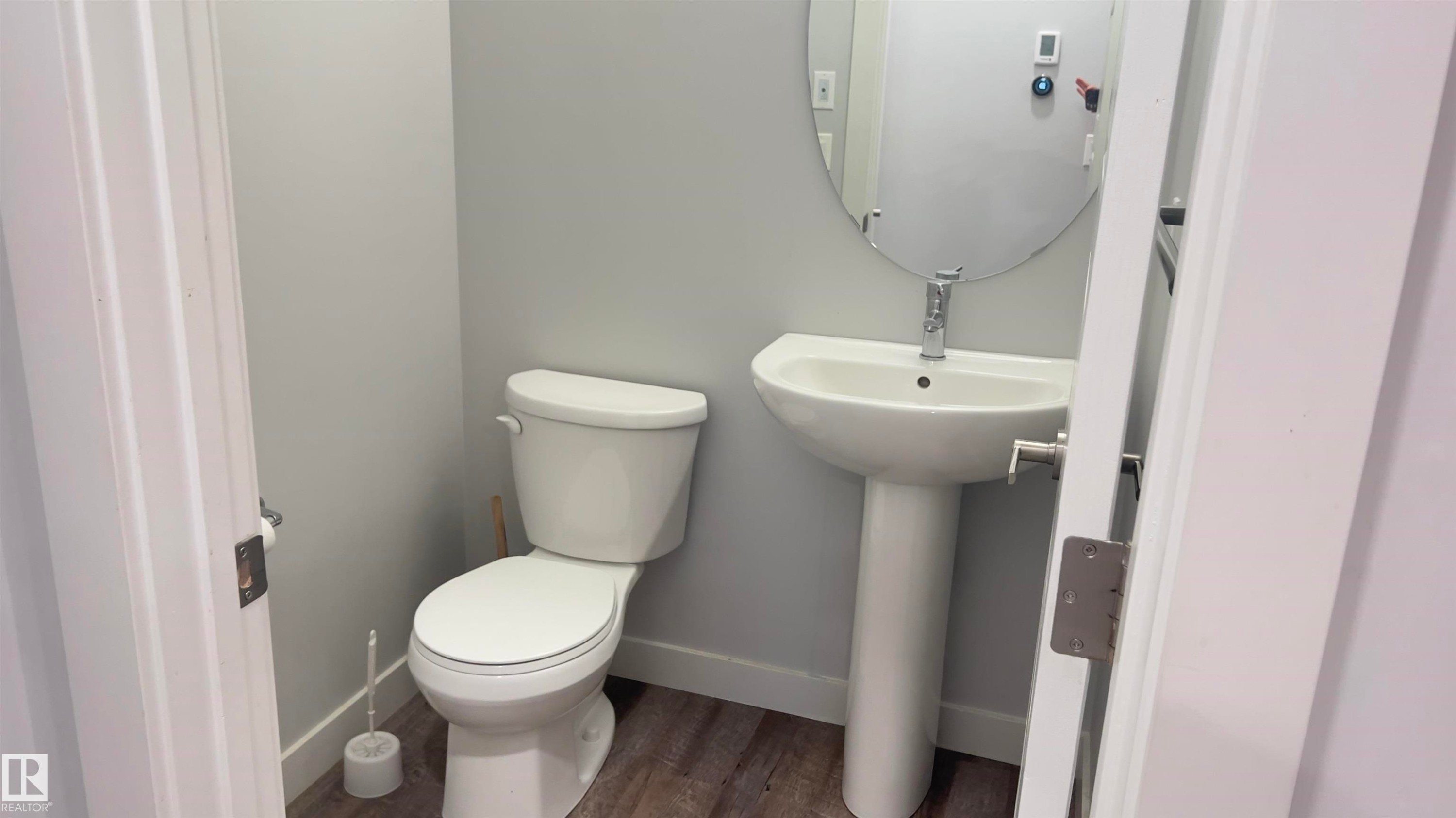 Pedestal sink with chrome faucet, oval mirror, and wood-finish flooring - 90 804 Welsh Drive, Edmonton, AB
