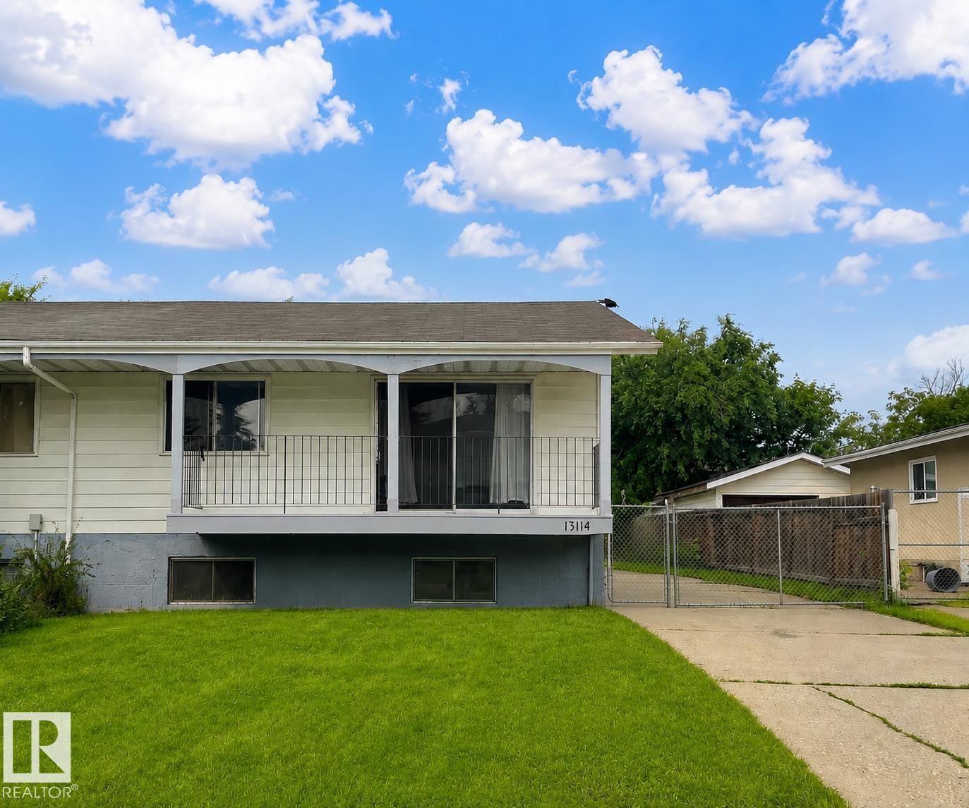 Exterior featuring a white siding finish, a covered balcony with black metal railings, sliding glass doors, a driveway, and a chain link fence - 13114 30 Street, Edmonton, AB - Outdoor With Deck Patio Veranda