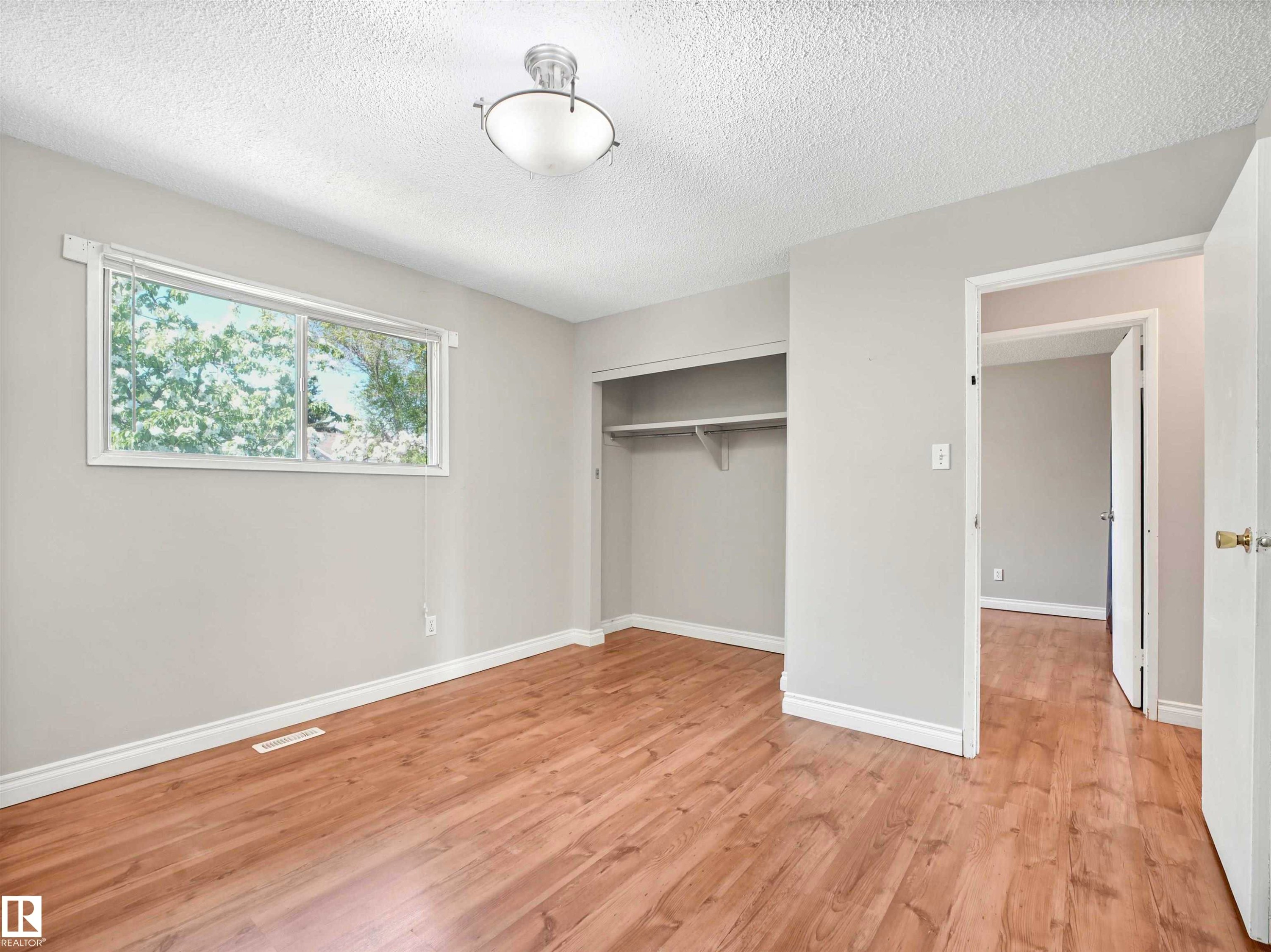 Room featuring wood-finish flooring, a double window, a ceiling-mounted light fixture, a built-in closet with shelving and hanging rod, and a doorway opening to an interior hallway - 13114 30 Street, Edmonton, AB - Indoor Photo Showing Other Room