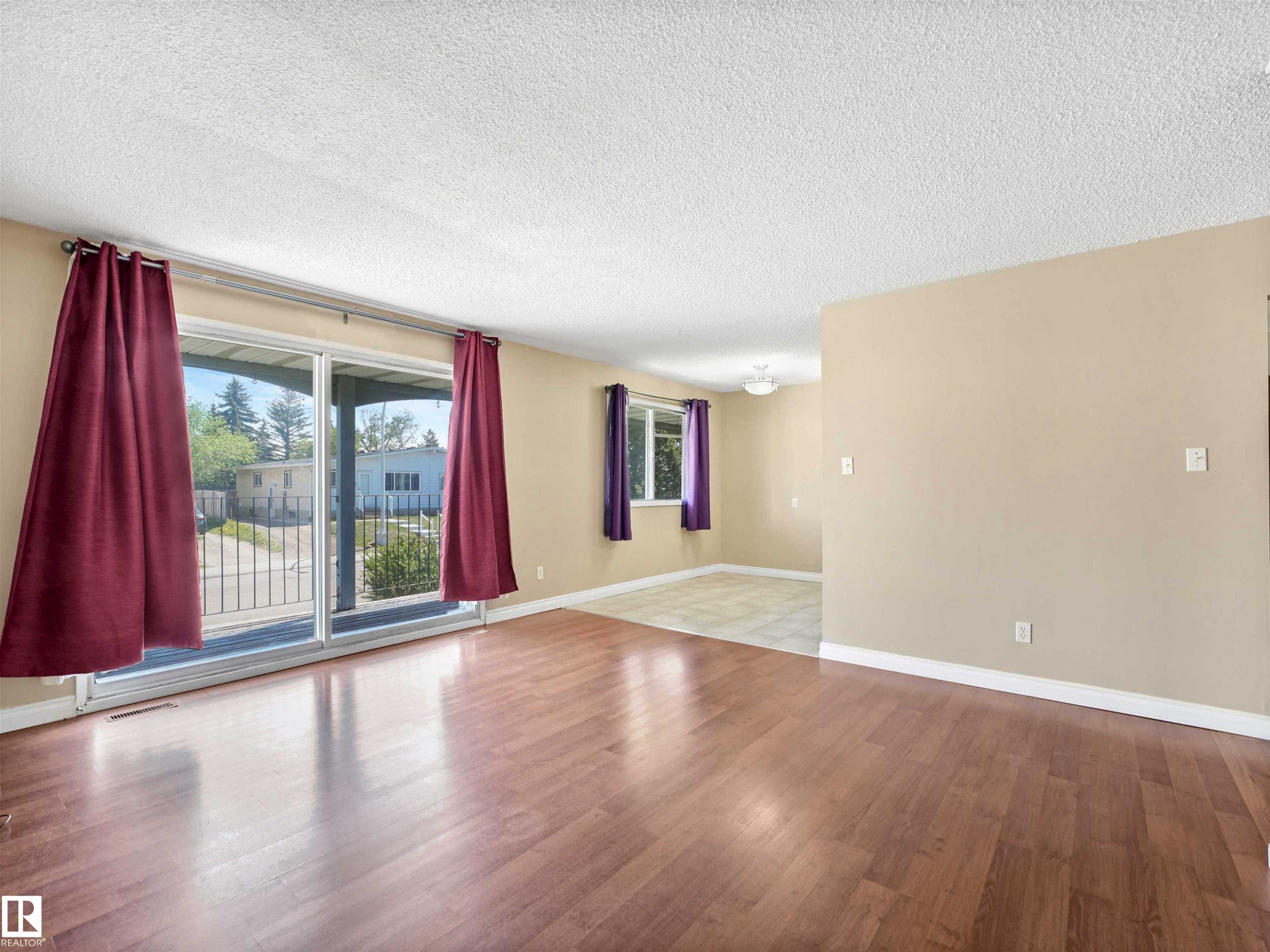 Spacious living area featuring wood-finish flooring, light tan wall paint, and white trim - 13114 30 Street, Edmonton, AB - Indoor Photo Showing Other Room