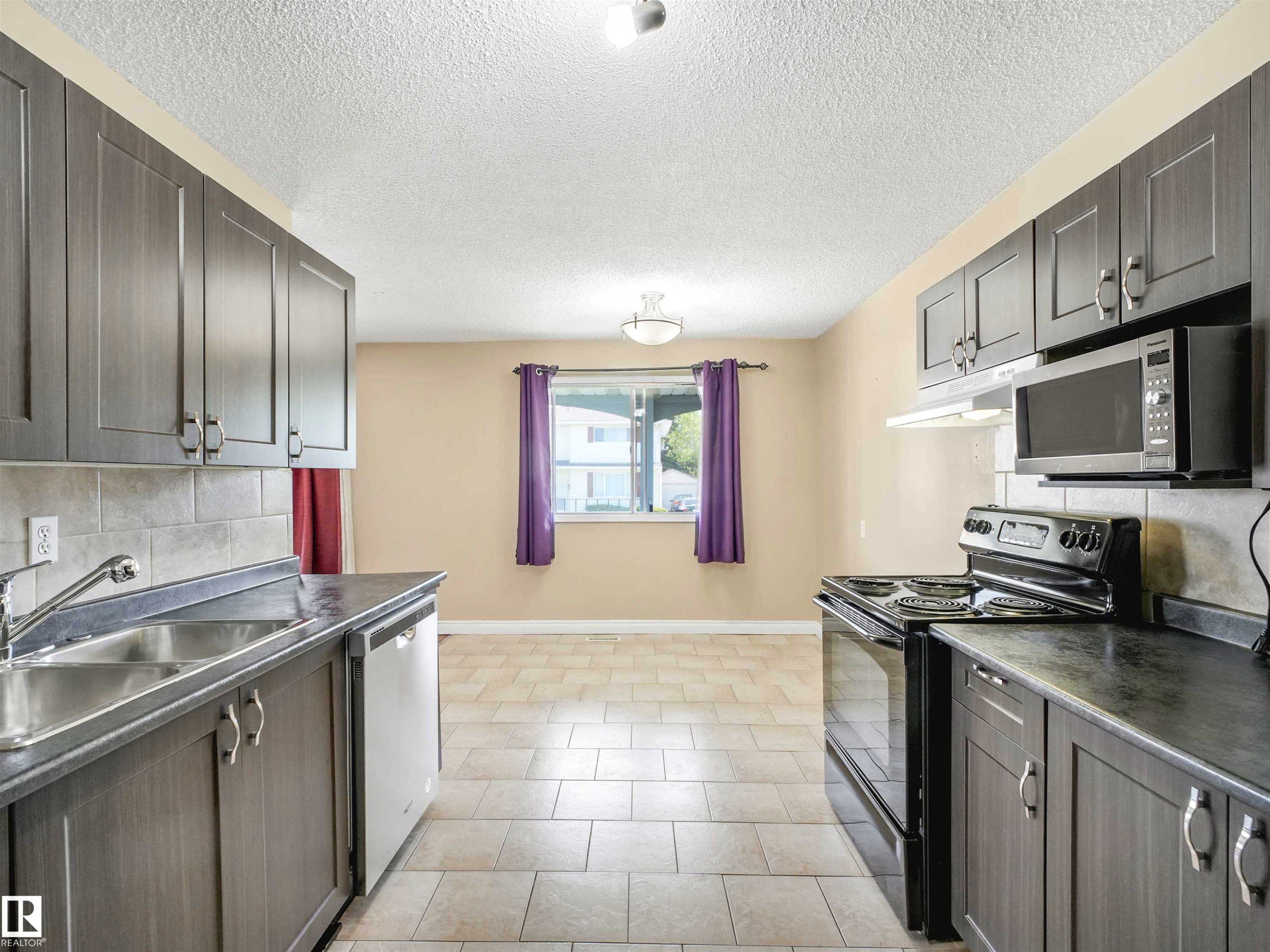 Kitchen with dark cabinetry, light countertops, and tile flooring - 13114 30 Street, Edmonton, AB - Indoor Photo Showing Kitchen With Double Sink