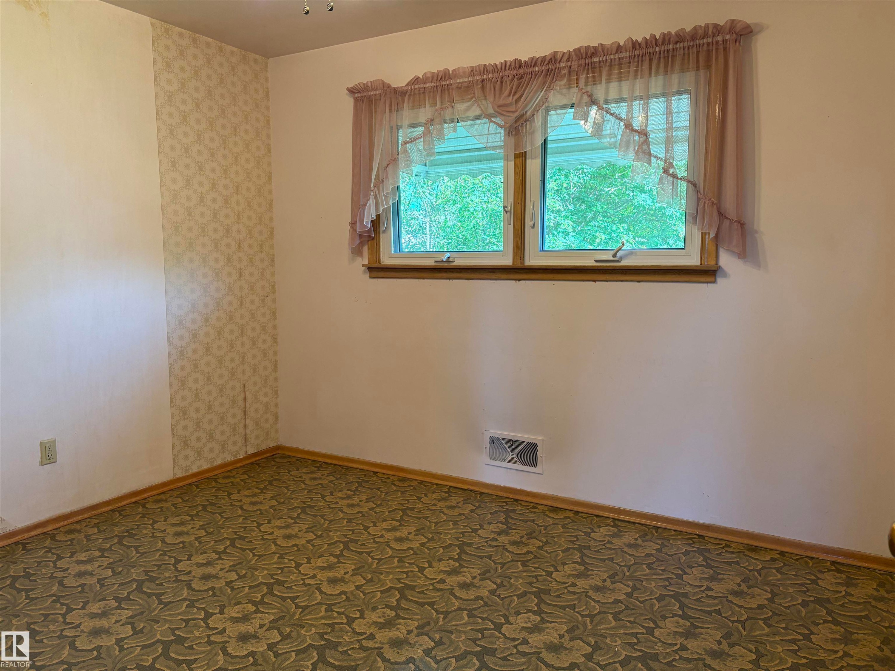 Room featuring a double-hung window with a wood frame, patterned wallpaper accent, baseboard trim, and floral-patterned carpeting - 5511 50 St, Tofield, AB