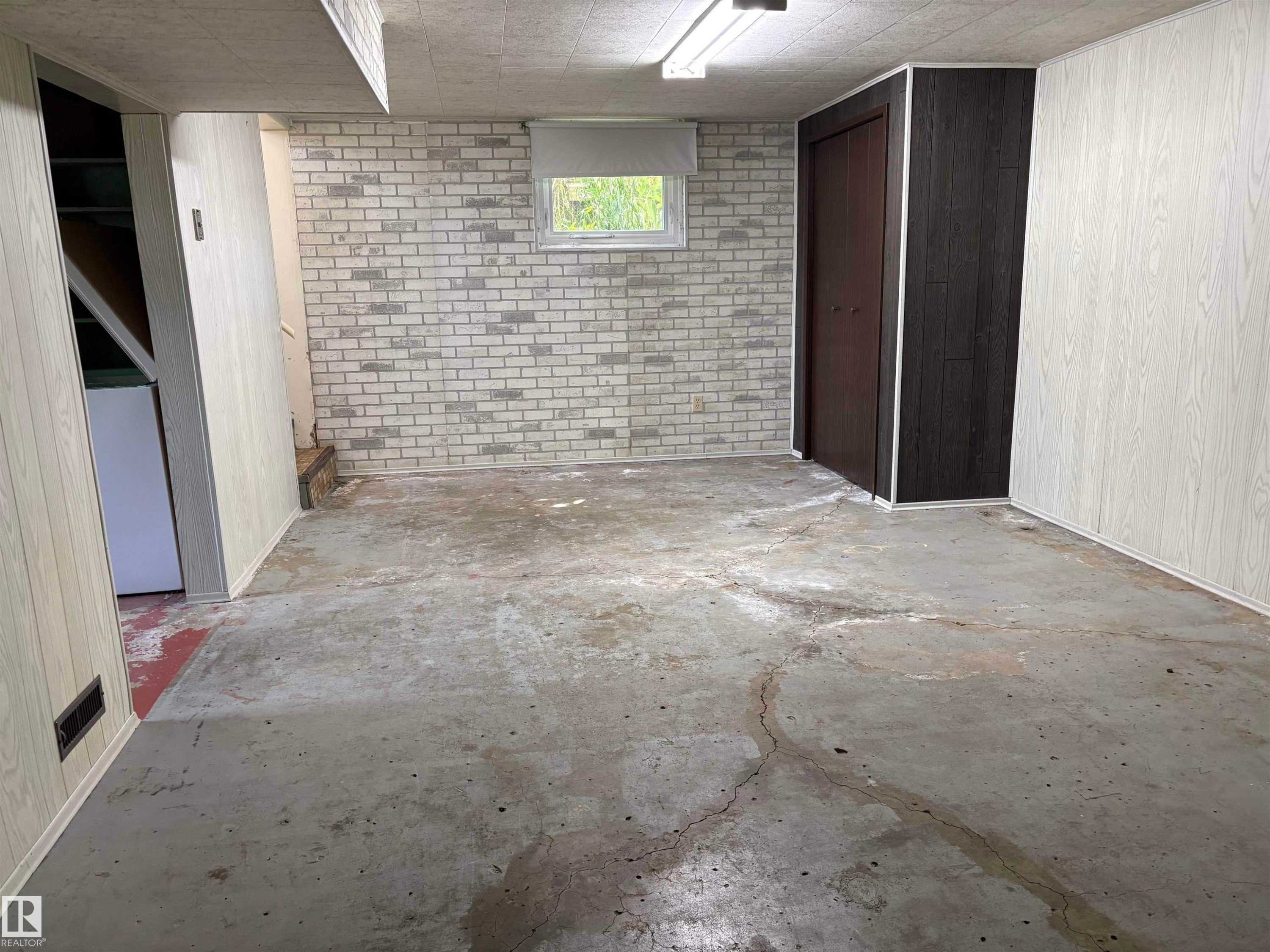 Finished basement space featuring a window, light-toned brick-patterned wall, and two-tone paneling - 5511 50 St, Tofield, AB