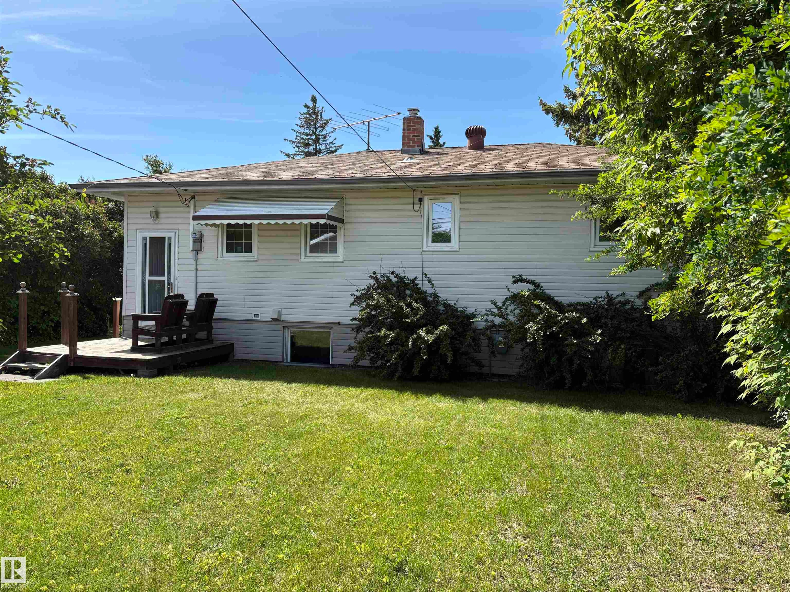 Spacious rear yard featuring a wood deck, mature landscaping, and light-colored siding - 5511 50 St, Tofield, AB