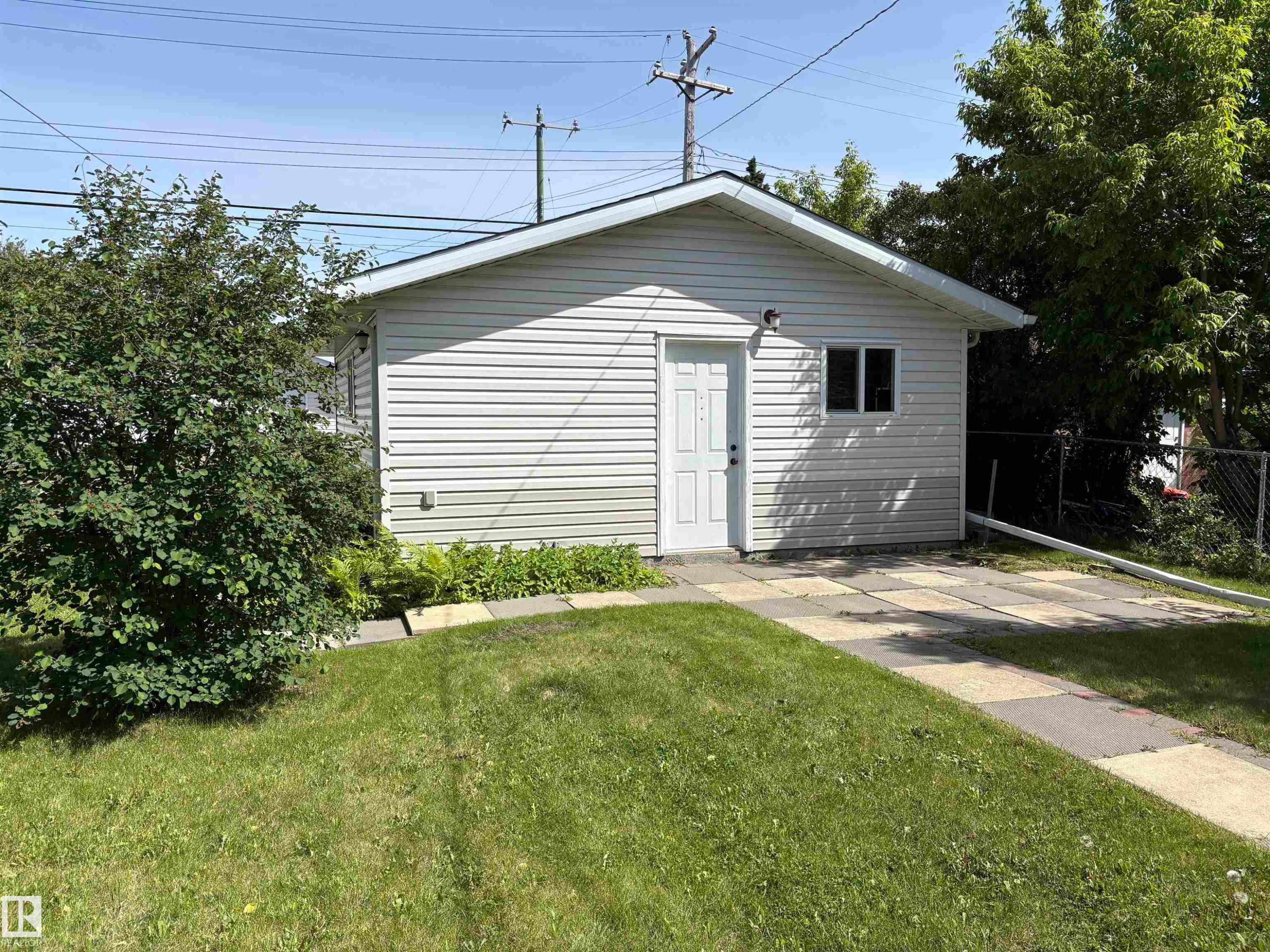 Detached garage featuring white vinyl siding, a white entry door, and a single window - 5511 50 St, Tofield, AB