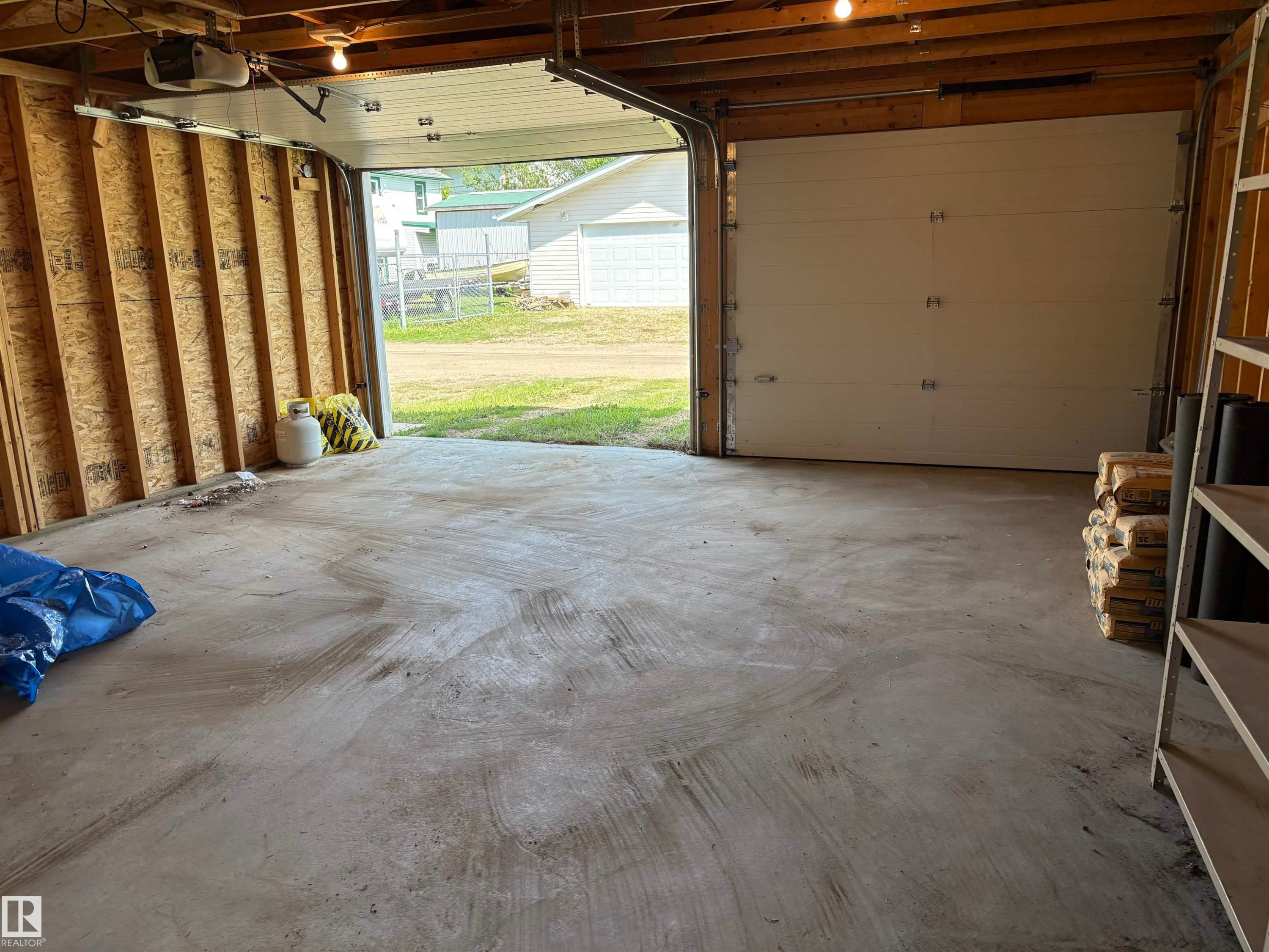 Concrete garage floor with exposed wood framing and a white panel garage door - 5511 50 St, Tofield, AB