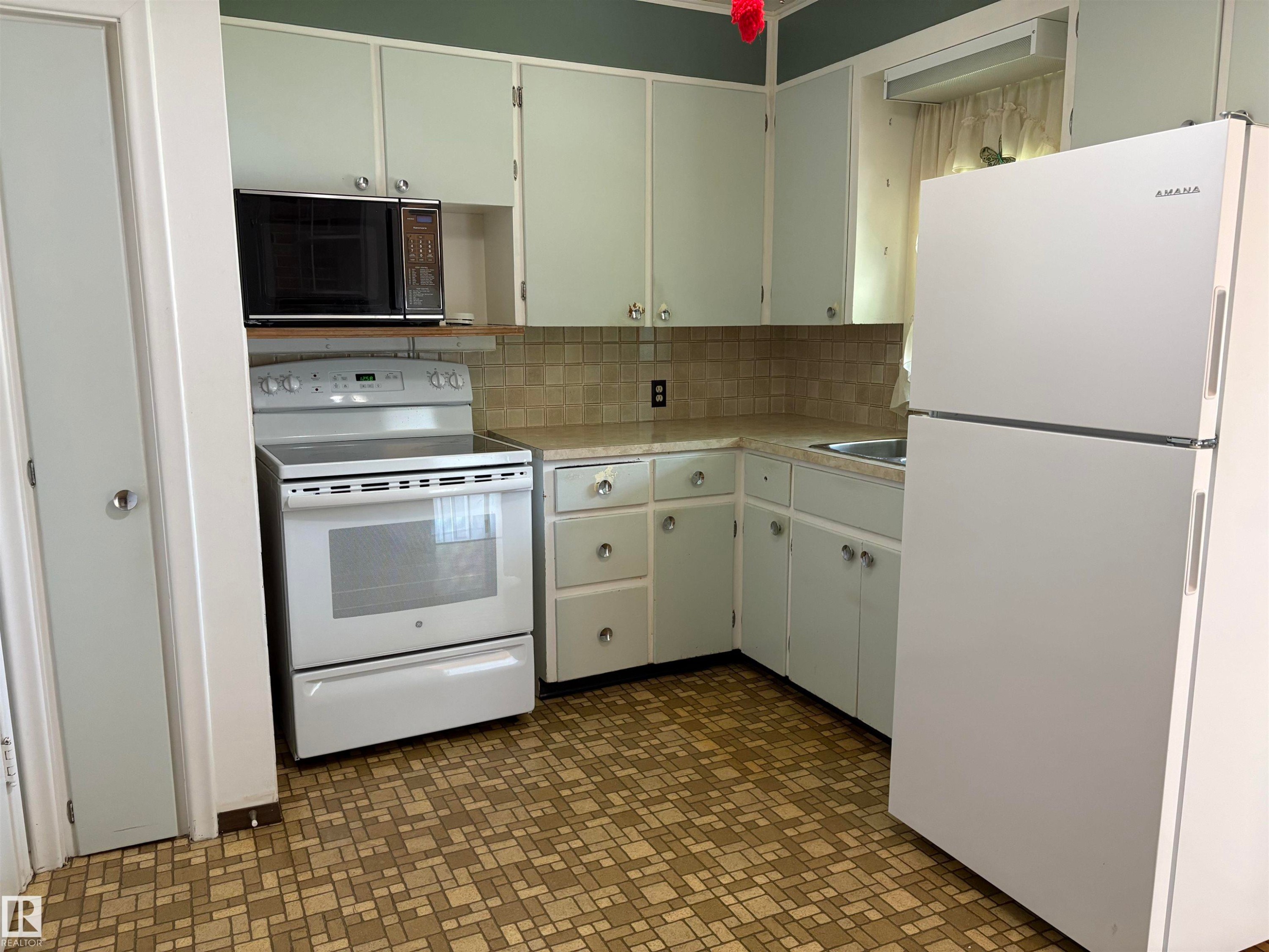 Kitchen featuring a white electric range, over-range microwave, and a white refrigerator - 5511 50 St, Tofield, AB
