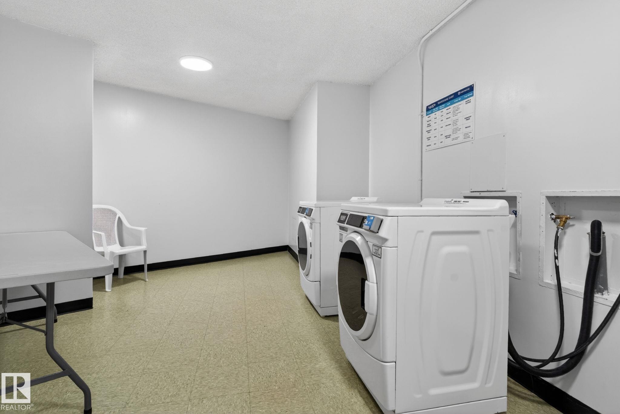 Dedicated laundry area featuring a white front-loading washing machine, light-colored flooring, and a round overhead light fixture - #412 13910 Stony Plain Rd Nw, Edmonton, AB - Indoor Photo Showing Laundry Room