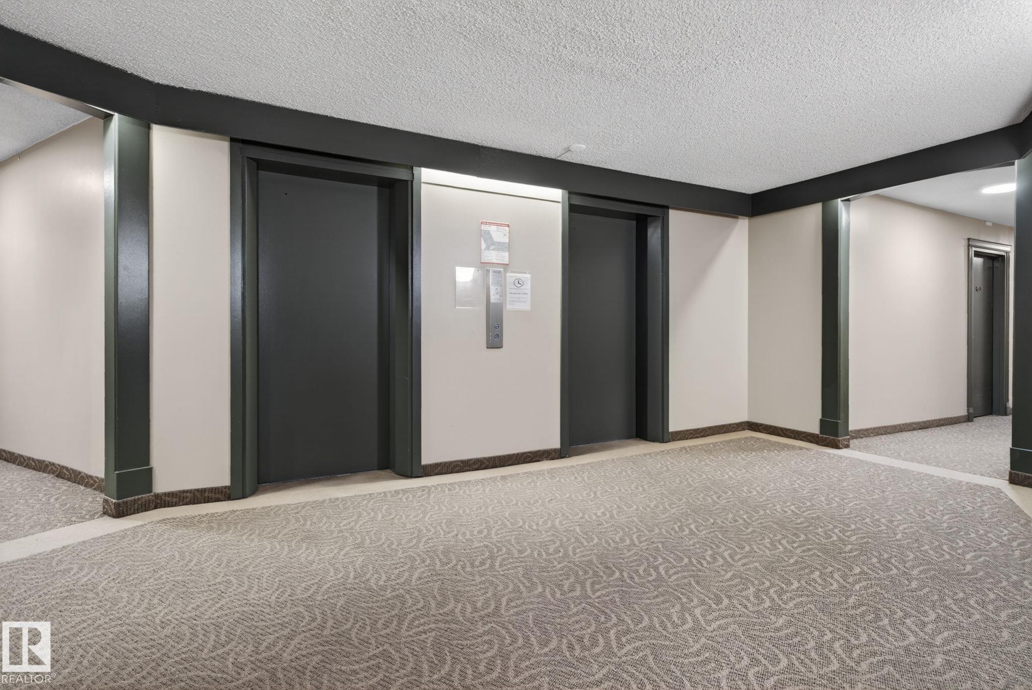 Building corridor featuring two elevators, textured carpet flooring, and a drop ceiling - #412 13910 Stony Plain Rd Nw, Edmonton, AB - Indoor Photo Showing Other Room