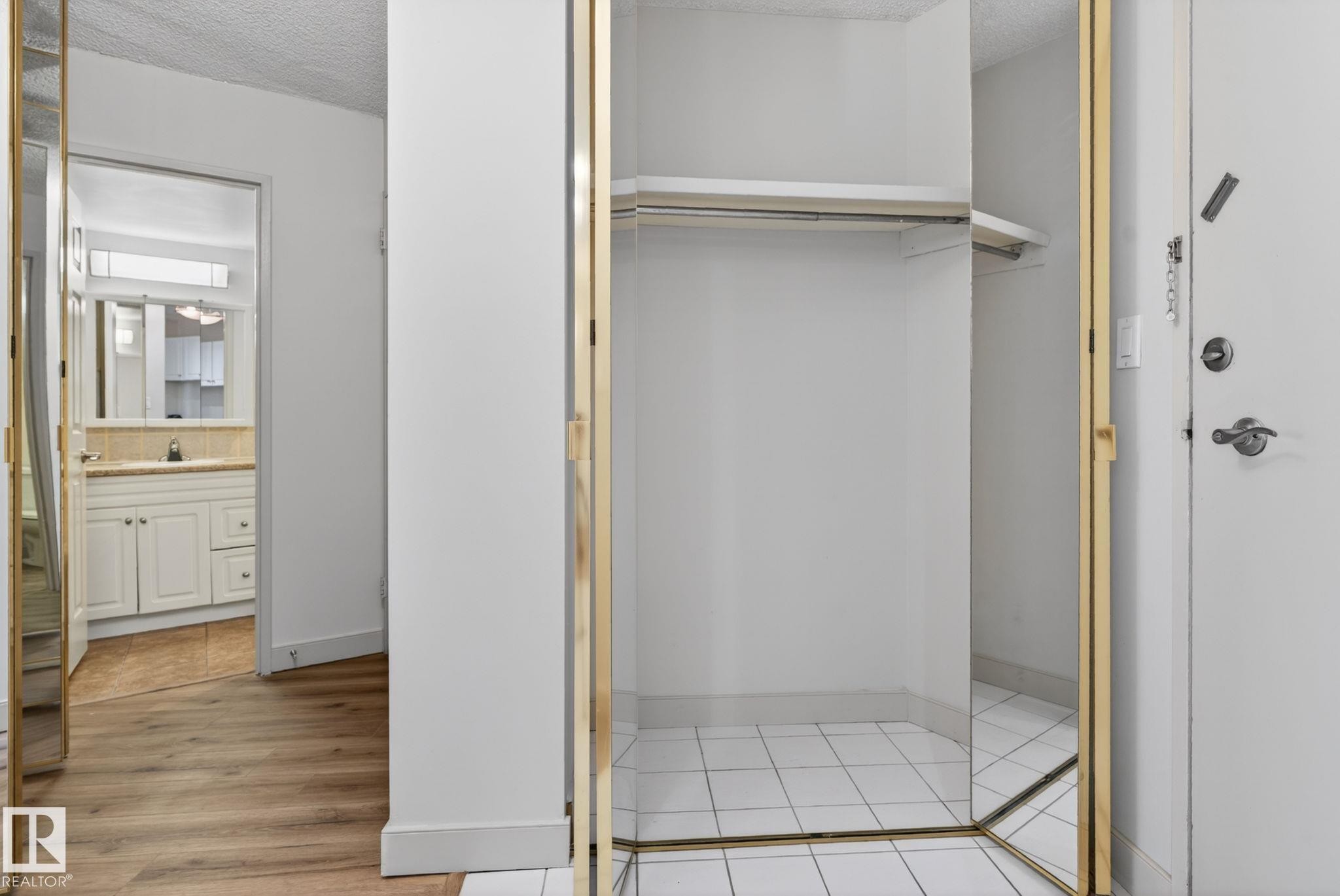 Mirrored bi-fold closet doors with gold-toned trim and white tile flooring - #412 13910 Stony Plain Rd Nw, Edmonton, AB - Indoor