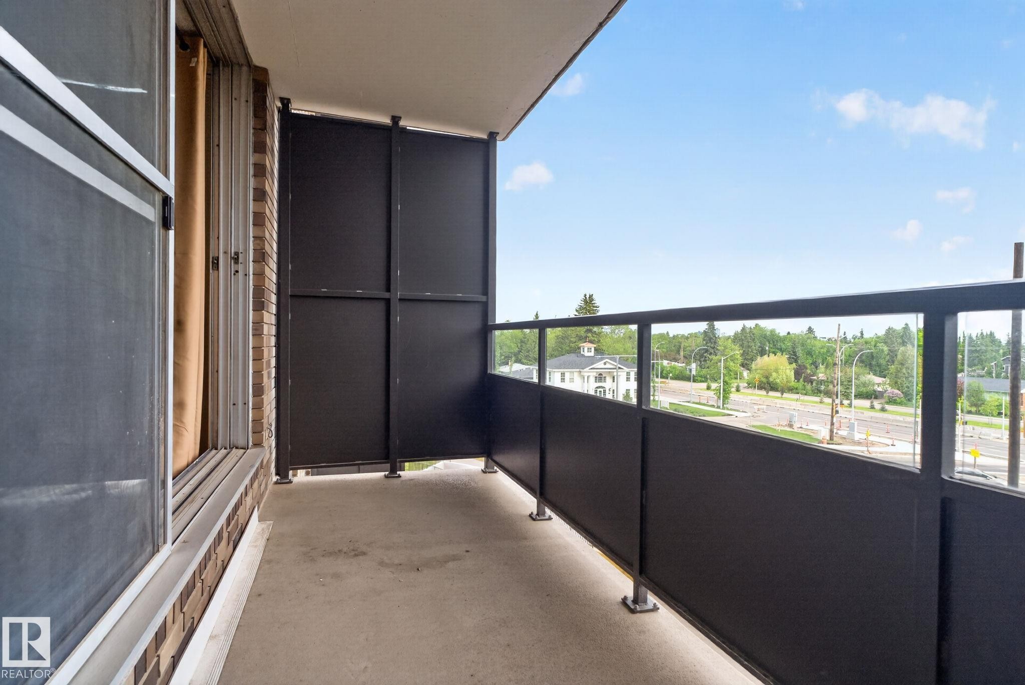 Private balcony featuring a concrete floor, dark privacy panels, and a glass-paneled railing - #412 13910 Stony Plain Rd Nw, Edmonton, AB - Outdoor With Balcony With Exterior
