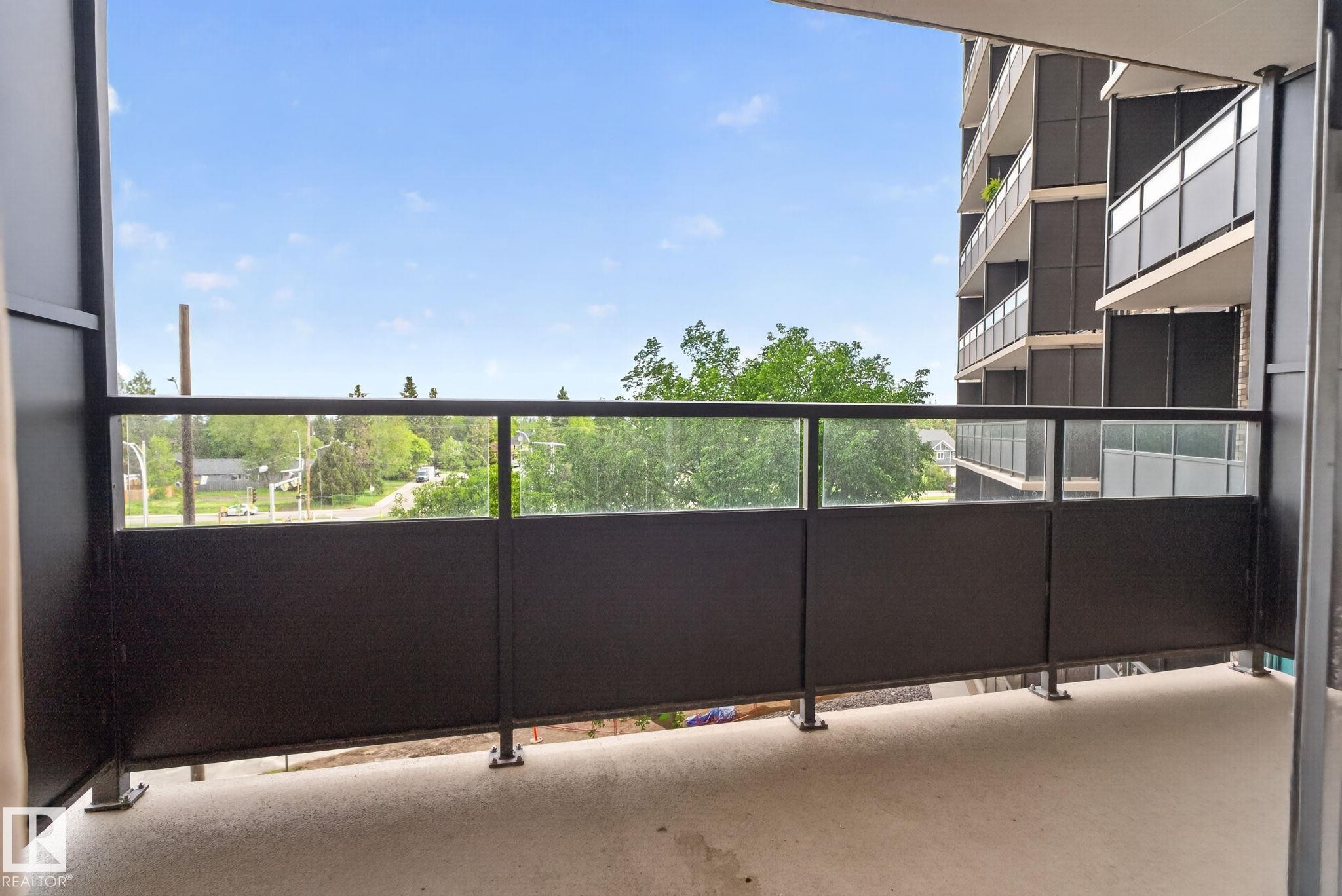 Private balcony featuring a concrete floor, black metal railings, and clear glass panels - #412 13910 Stony Plain Rd Nw, Edmonton, AB - Outdoor With Balcony With Exterior