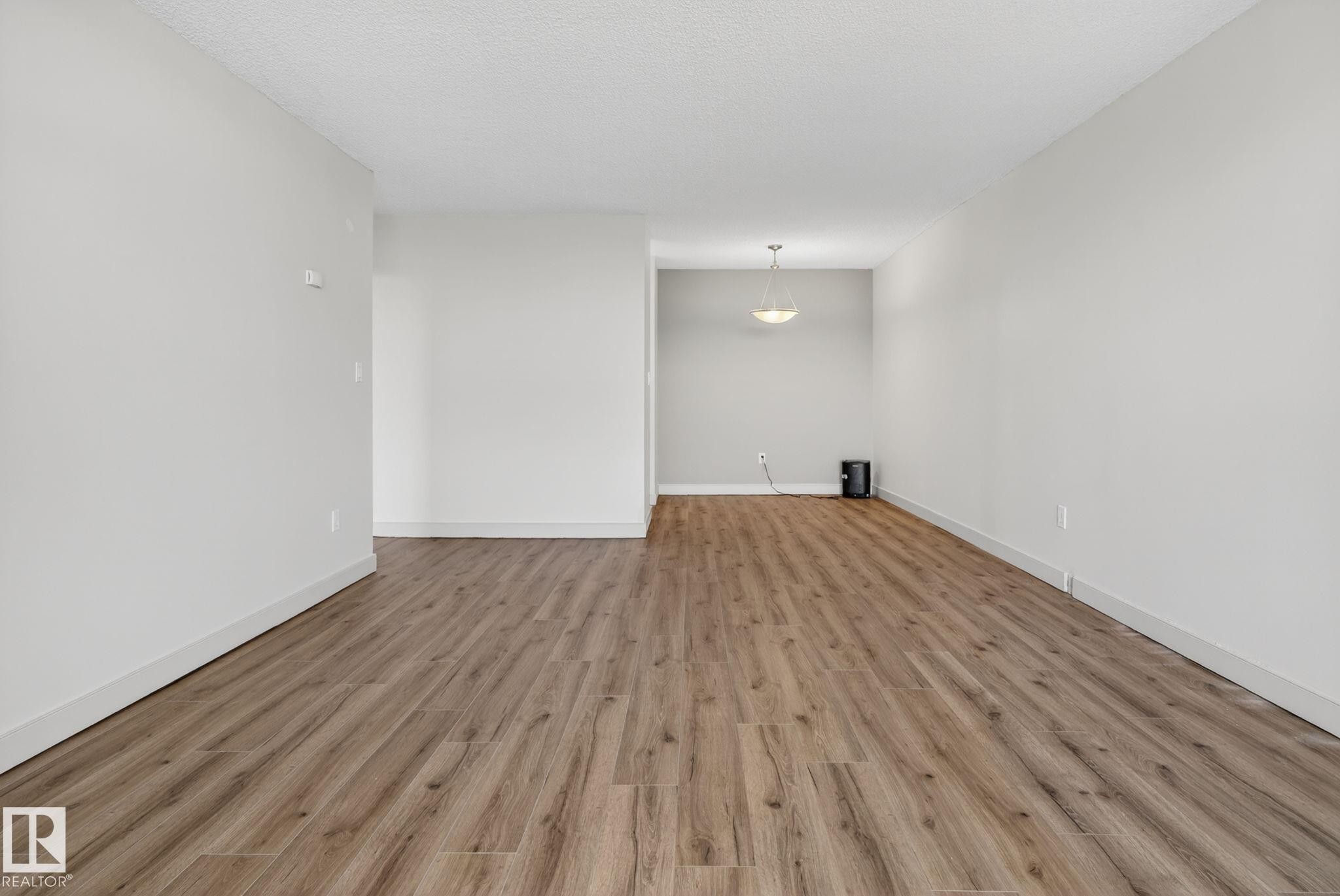 Open-concept living area featuring wood-finish flooring, white baseboards, and neutral wall paint - #412 13910 Stony Plain Rd Nw, Edmonton, AB - Indoor Photo Showing Other Room
